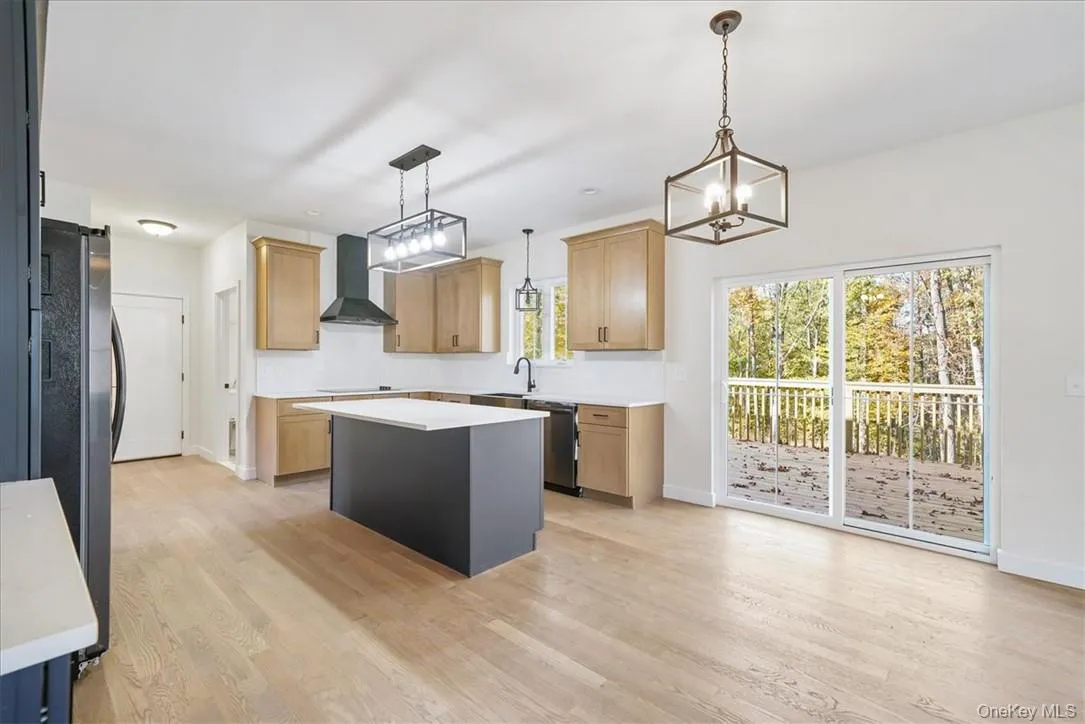 Kitchen featuring appliances with stainless steel finishes, hanging light fixtures, wall chimney range hood, and a kitchen island Kitchen featuring appliances with stainless steel finishes, hanging light fixtures, wall chimney range hood, and a kitchen island