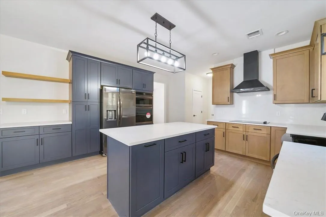 Kitchen featuring wall chimney exhaust hood, light wood-type flooring, pendant lighting, a kitchen island, and black appliances Kitchen featuring wall chimney exhaust hood, light wood-type flooring, pendant lighting, a kitchen island, and black appliances