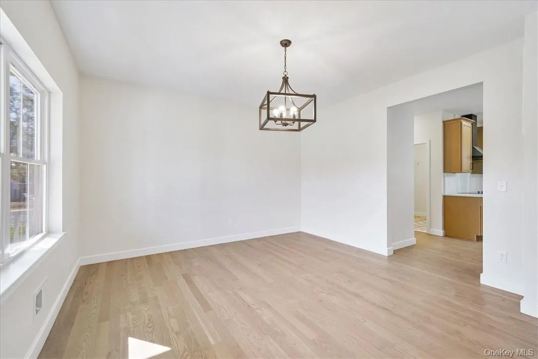 Unfurnished room featuring plenty of natural light, a notable chandelier, and light wood-type flooring Unfurnished room featuring plenty of natural light, a notable chandelier, and light wood-type flooring