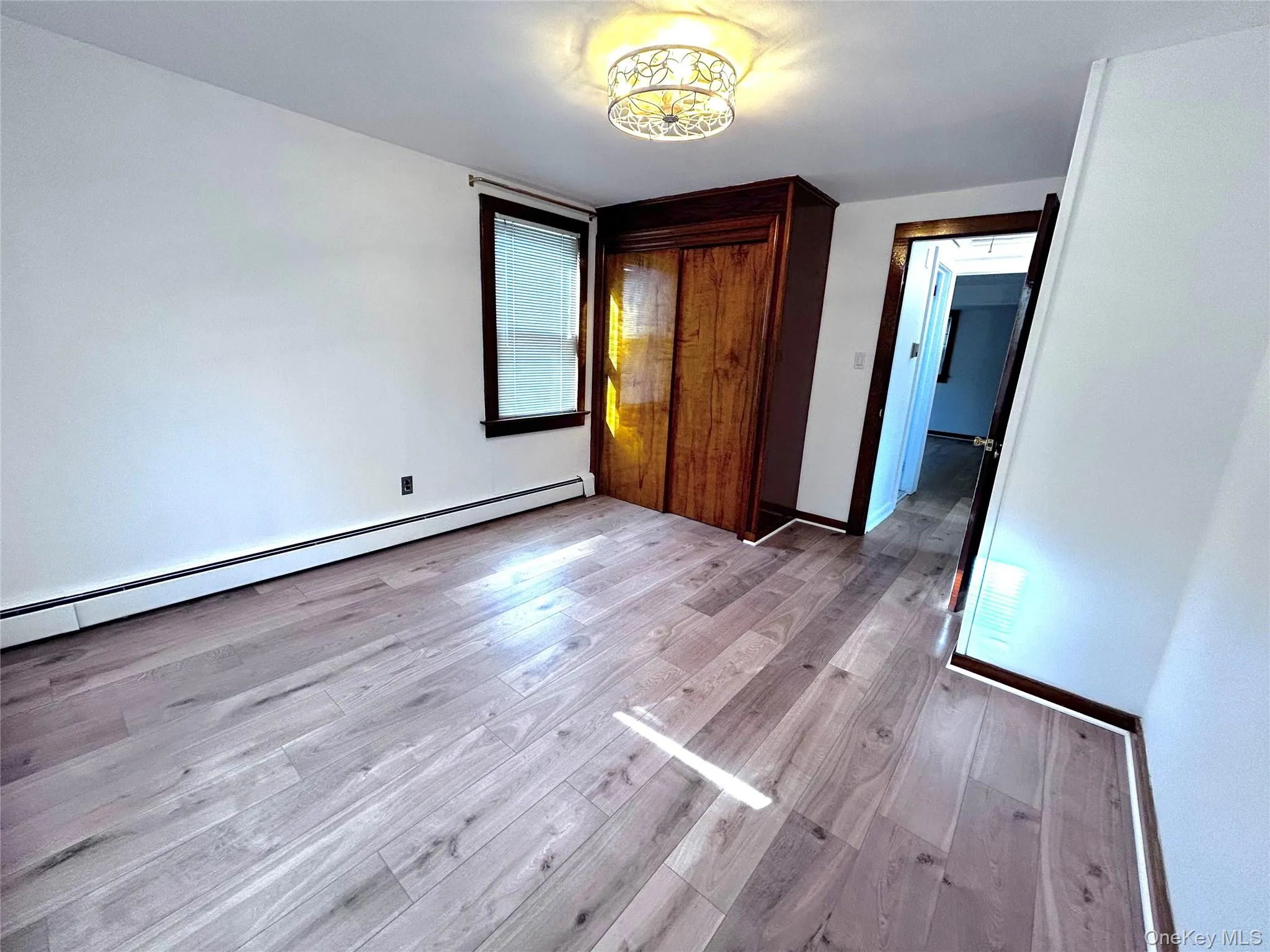 Unfurnished bedroom featuring a baseboard radiator, a closet, and light wood-style flooring Unfurnished bedroom featuring a baseboard radiator, a closet, and light wood-style flooring