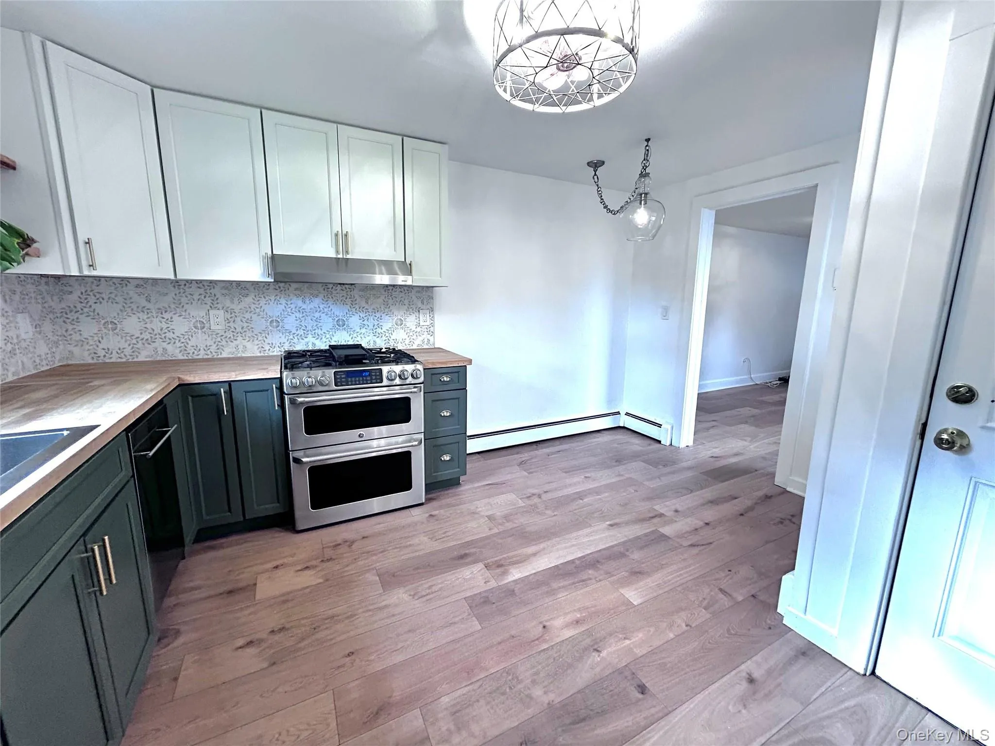 Kitchen with white cabinetry, tasteful backsplash, stainless steel appliances, decorative light fixtures, and light wood finished floors Kitchen with white cabinetry, tasteful backsplash, stainless steel appliances, decorative light fixtures, and light wood finished floors