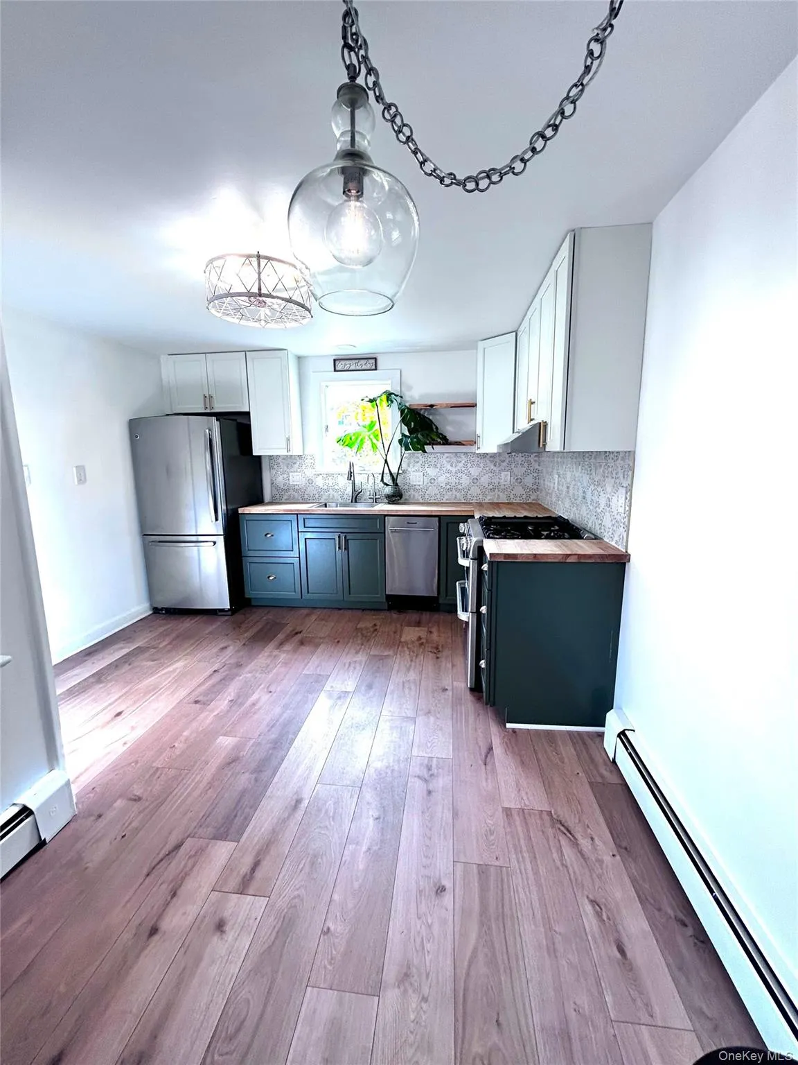 Kitchen with a baseboard radiator, white cabinets, appliances with stainless steel finishes, and light wood-style flooring Kitchen with a baseboard radiator, white cabinets, appliances with stainless steel finishes, and light wood-style flooring