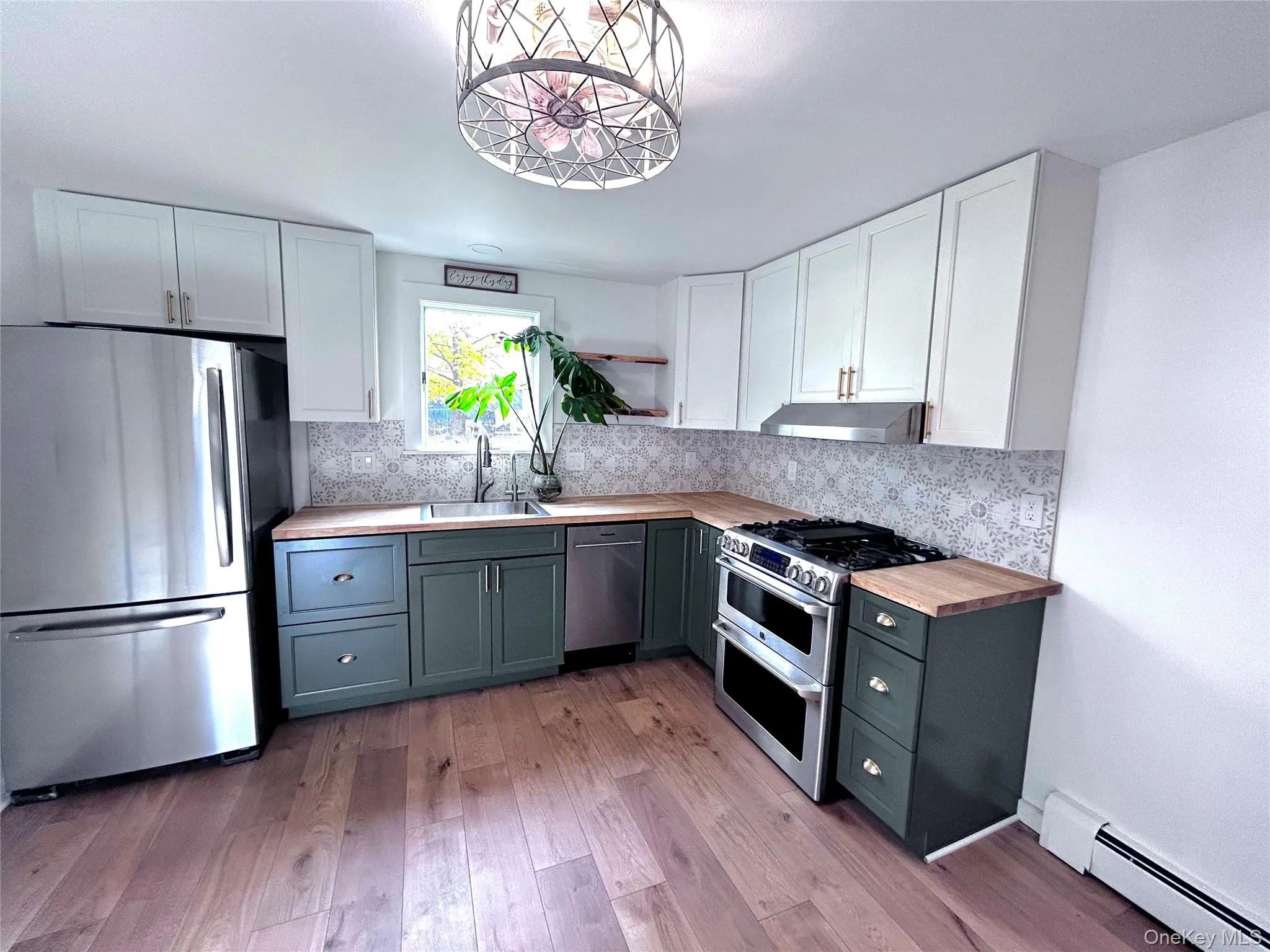 Kitchen featuring white cabinetry, appliances with stainless steel finishes, wooden counters, a baseboard radiator, and tasteful backsplash Kitchen featuring white cabinetry, appliances with stainless steel finishes, wooden counters, a baseboard radiator, and tasteful backsplash