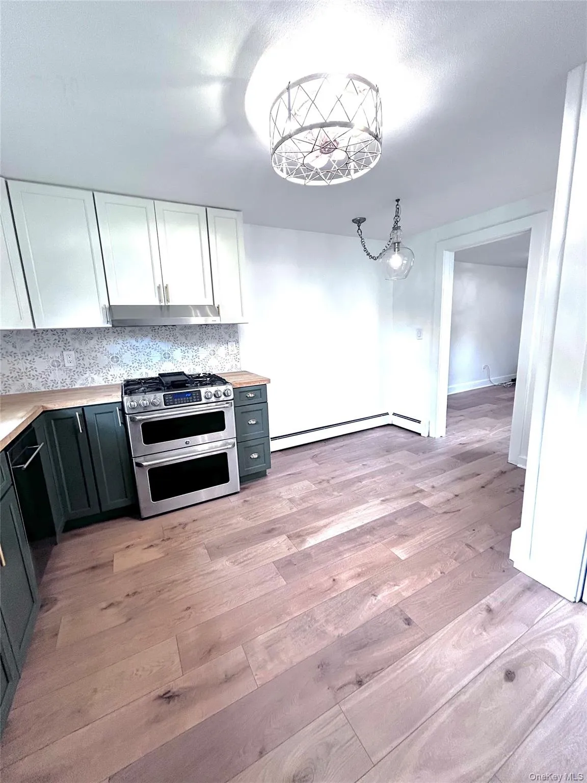 Kitchen with double oven range, light countertops, white cabinets, decorative backsplash, and decorative light fixtures Kitchen with double oven range, light countertops, white cabinets, decorative backsplash, and decorative light fixtures