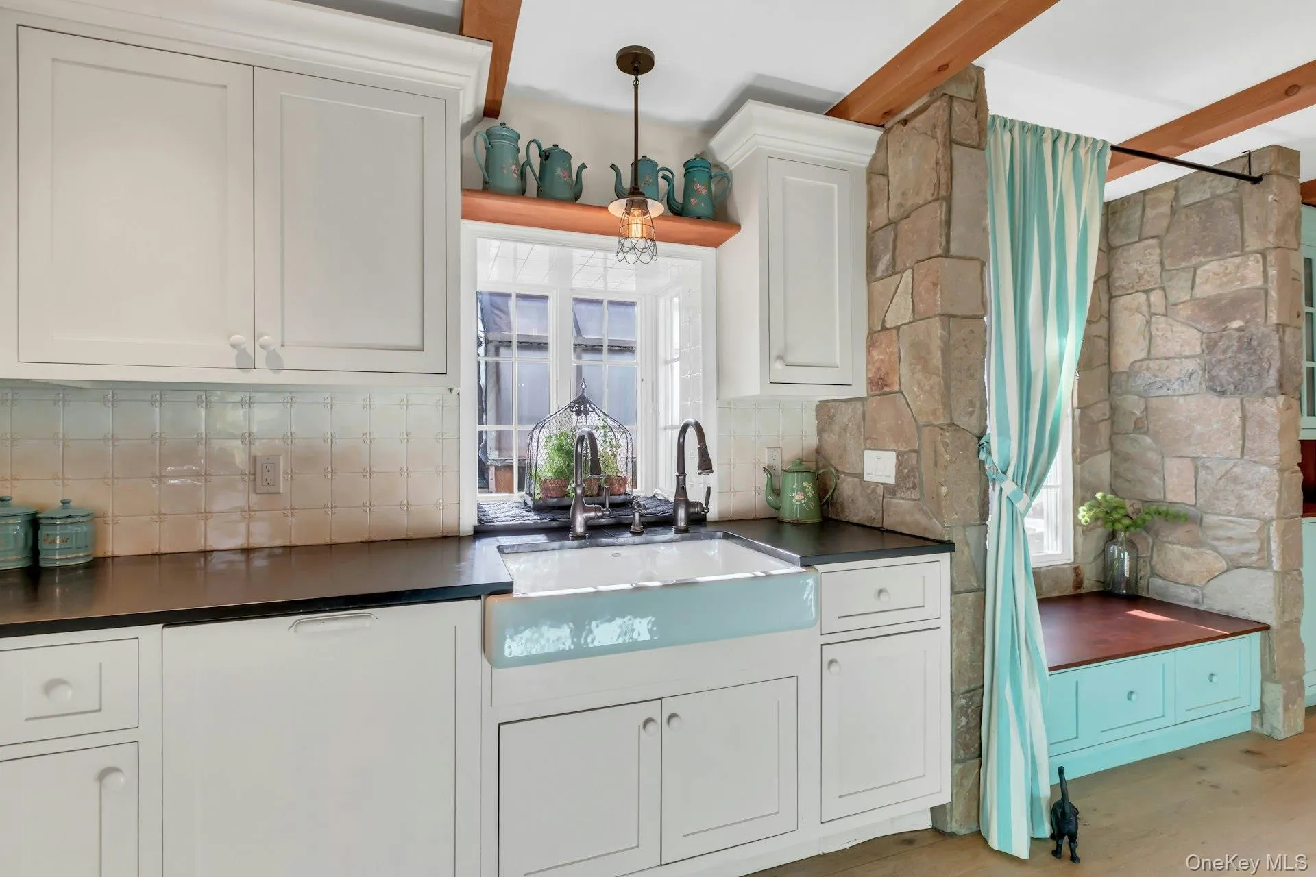 Kitchen featuring dark countertops, white cabinetry, tasteful backsplash, light wood finished floors, and decorative light fixtures Kitchen featuring dark countertops, white cabinetry, tasteful backsplash, light wood finished floors, and decorative light fixtures