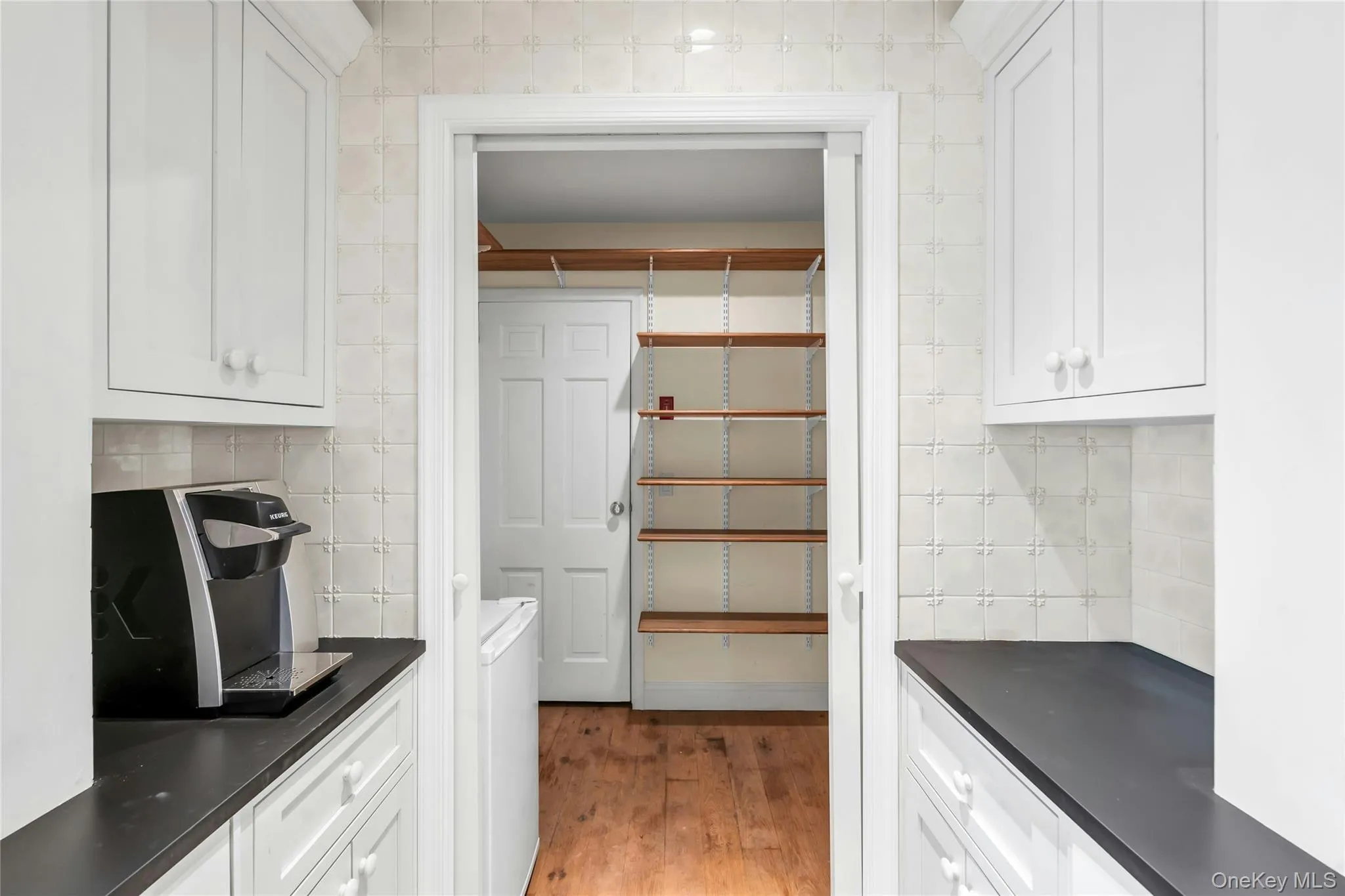 Galley-style utility space featuring upper and lower white cabinetry, dark stone countertops and a handmade decorative tiled backsplash Galley-style utility space featuring upper and lower white cabinetry, dark stone countertops and a handmade decorative tiled backsplash