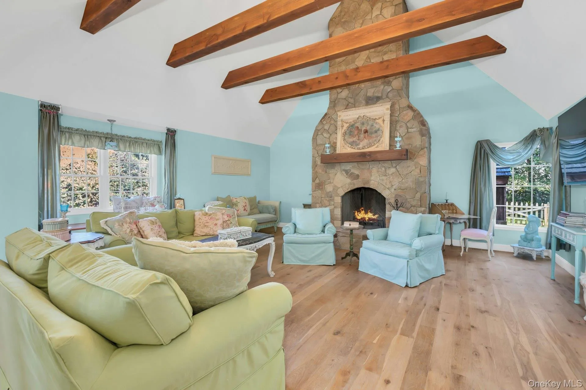 Staged Great room living area with high vaulted ceiling, a stone fireplace, light wood-type flooring, healthy amount of natural light, and beamed ceiling Staged Great room living area with high vaulted ceiling, a stone fireplace, light wood-type flooring, healthy amount of natural light, and beamed ceiling