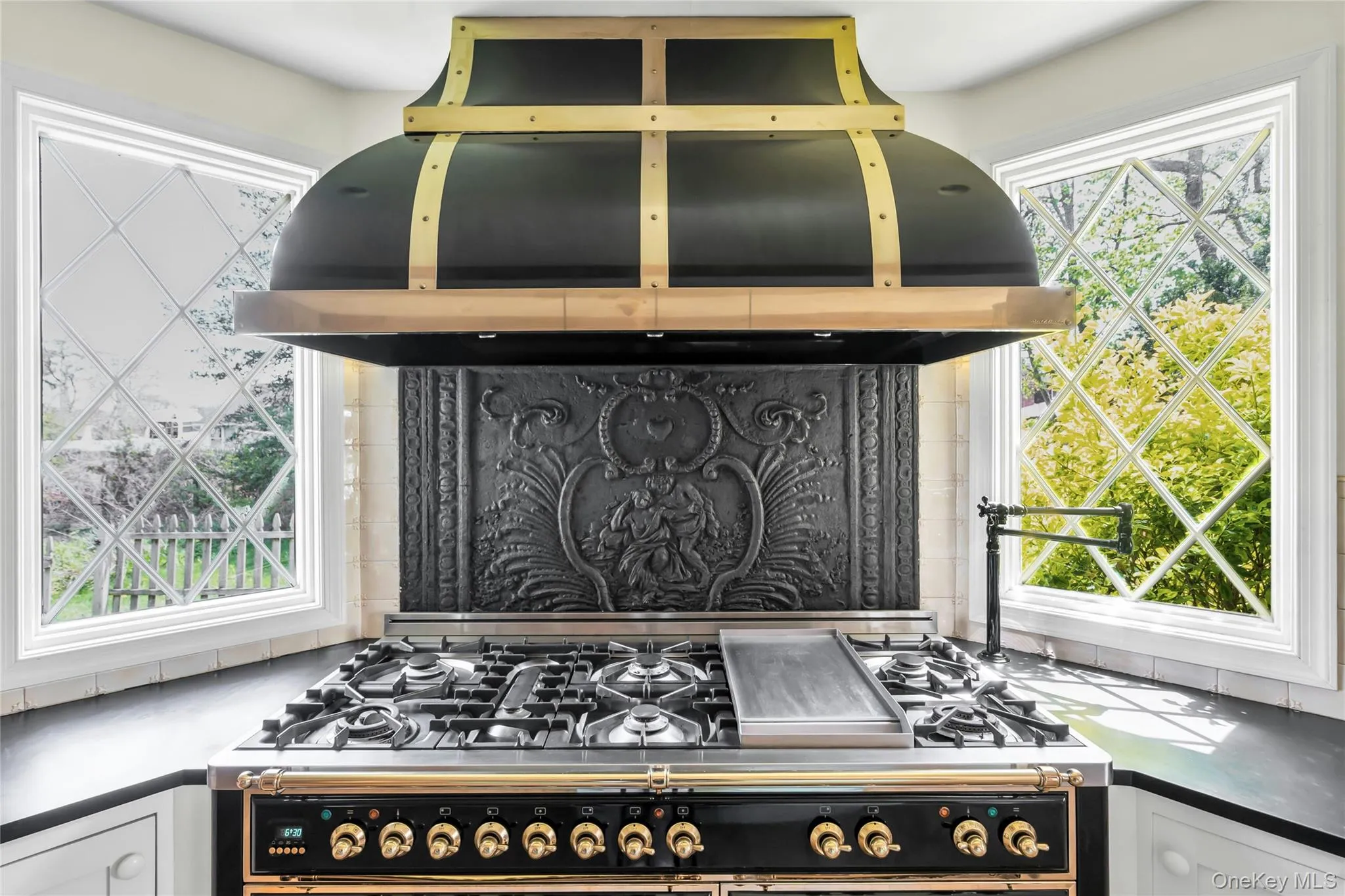 Professional-grade range with a custom black and brass vent hood, ornate cast-iron backsplash, and pot filler Professional-grade range with a custom black and brass vent hood, ornate cast-iron backsplash, and pot filler