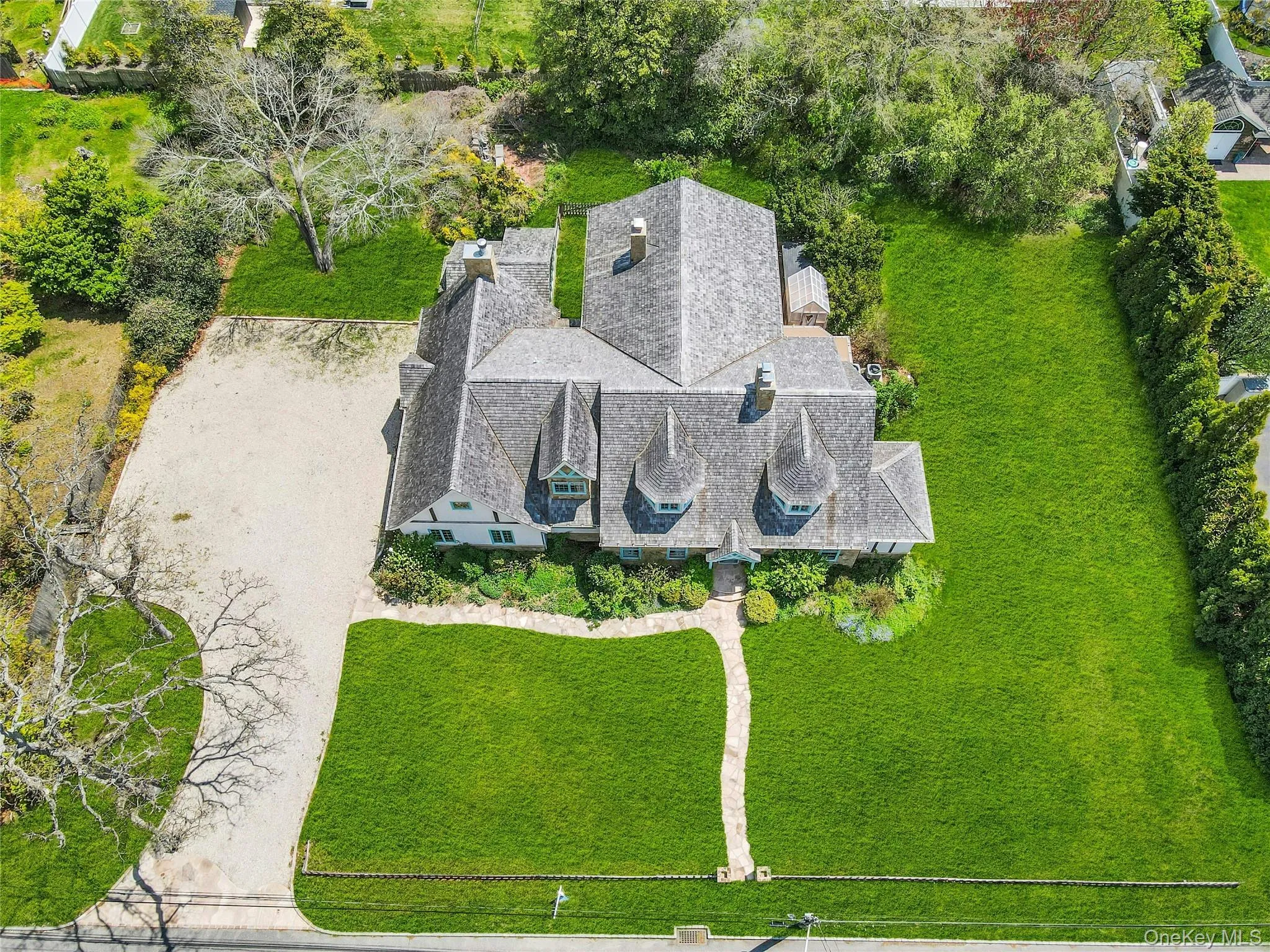 Exterior featuring a multi-gabled roof, three turret-style dormers, extensive lawn, a stone pathway, and a gravel driveway Exterior featuring a multi-gabled roof, three turret-style dormers, extensive lawn, a stone pathway, and a gravel driveway