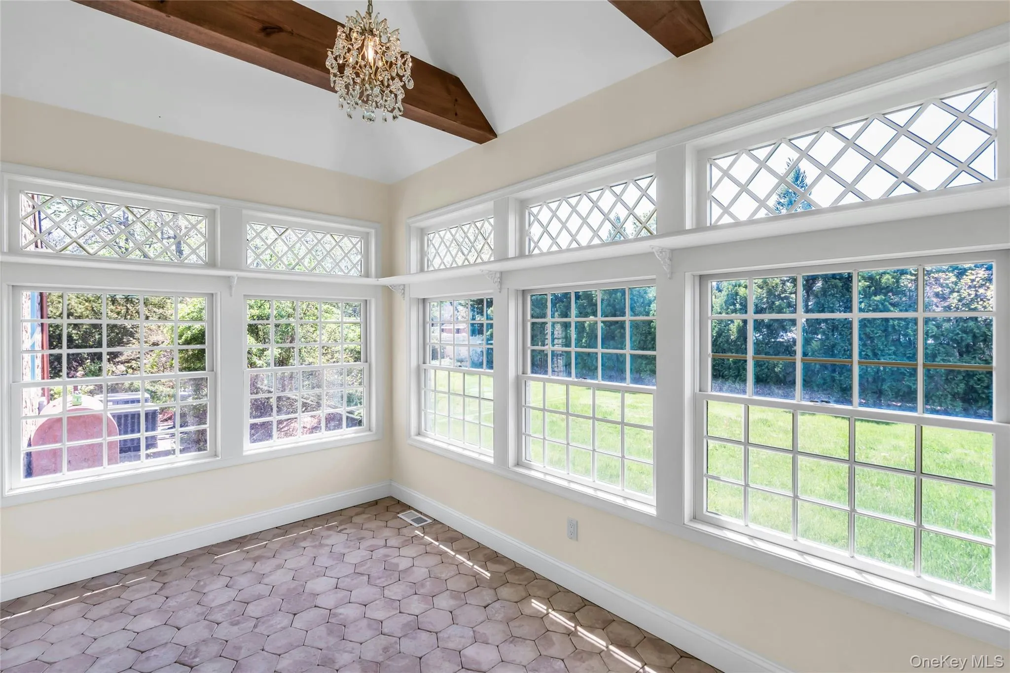 Sunroom with imported hexagonal tile flooring, exposed wood ceiling beams, and a crystal chandelier Sunroom with imported hexagonal tile flooring, exposed wood ceiling beams, and a crystal chandelier