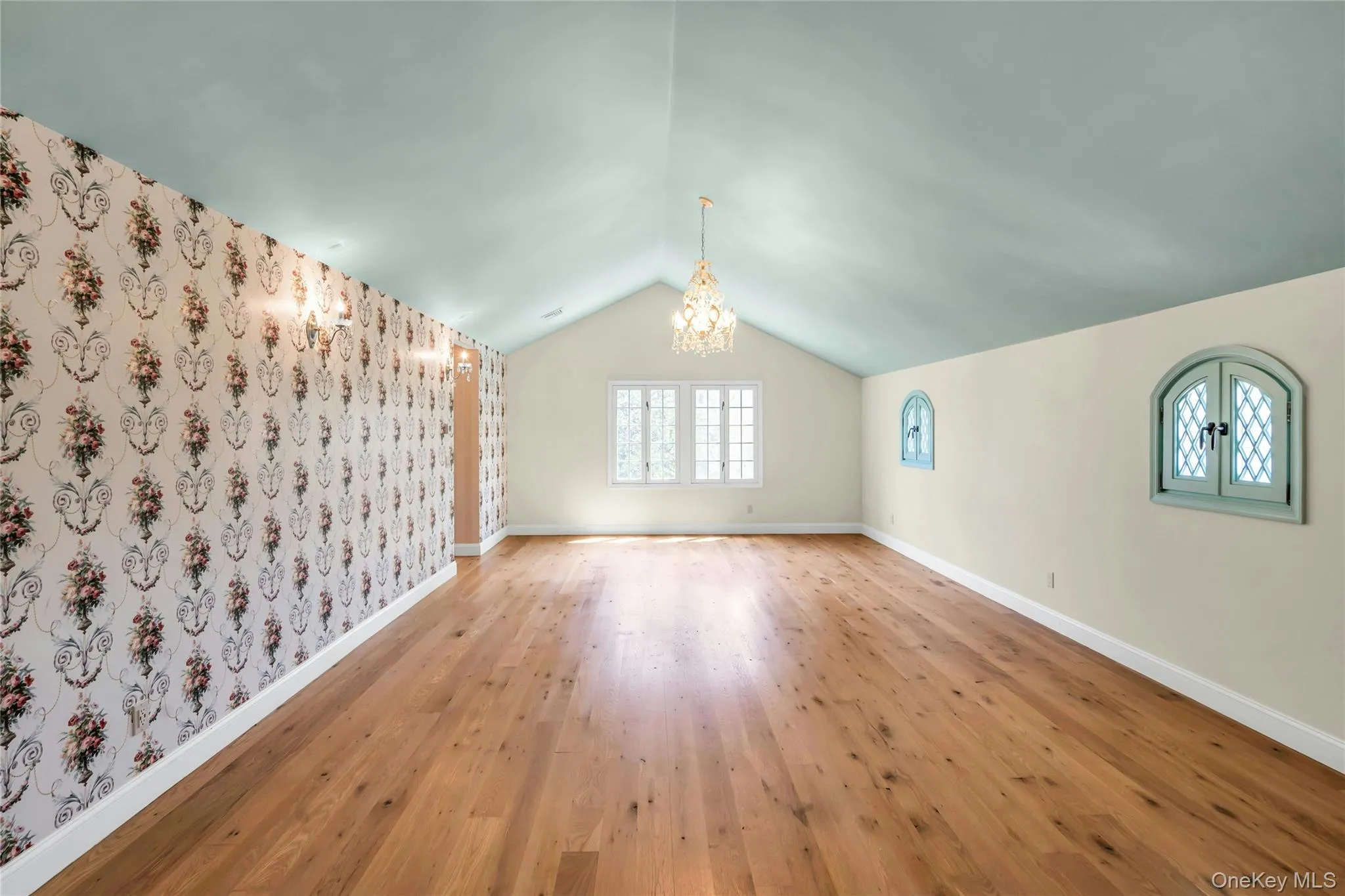 Spacious interior featuring 2 Parrett windows, wood-finish flooring, a vaulted ceiling, wall sconces and a decorative chandelier Spacious interior featuring 2 Parrett windows, wood-finish flooring, a vaulted ceiling, wall sconces and a decorative chandelier
