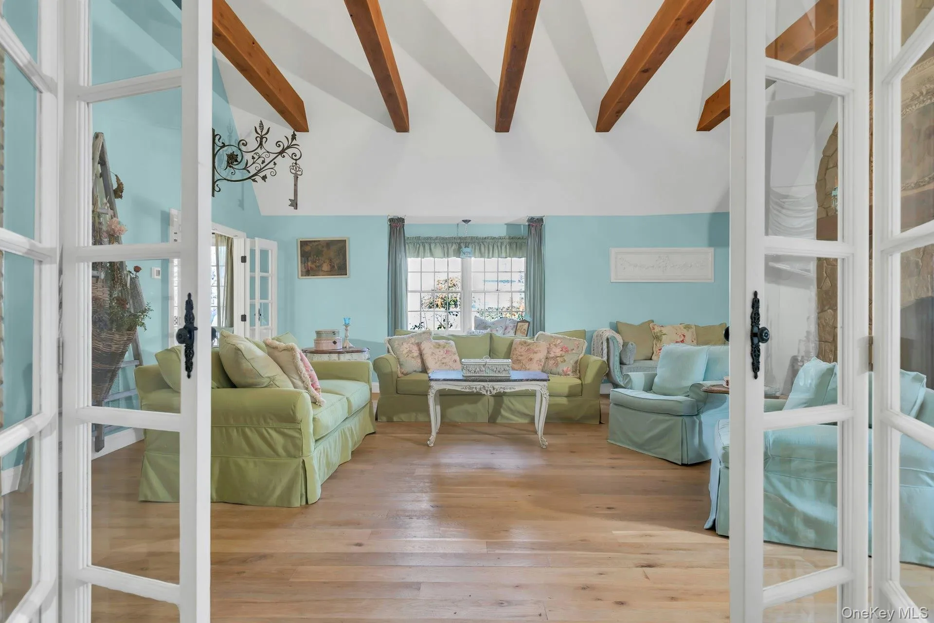 Staged great room with high vaulted ceiling, beam ceiling, light wood-style flooring, and french doors Staged great room with high vaulted ceiling, beam ceiling, light wood-style flooring, and french doors