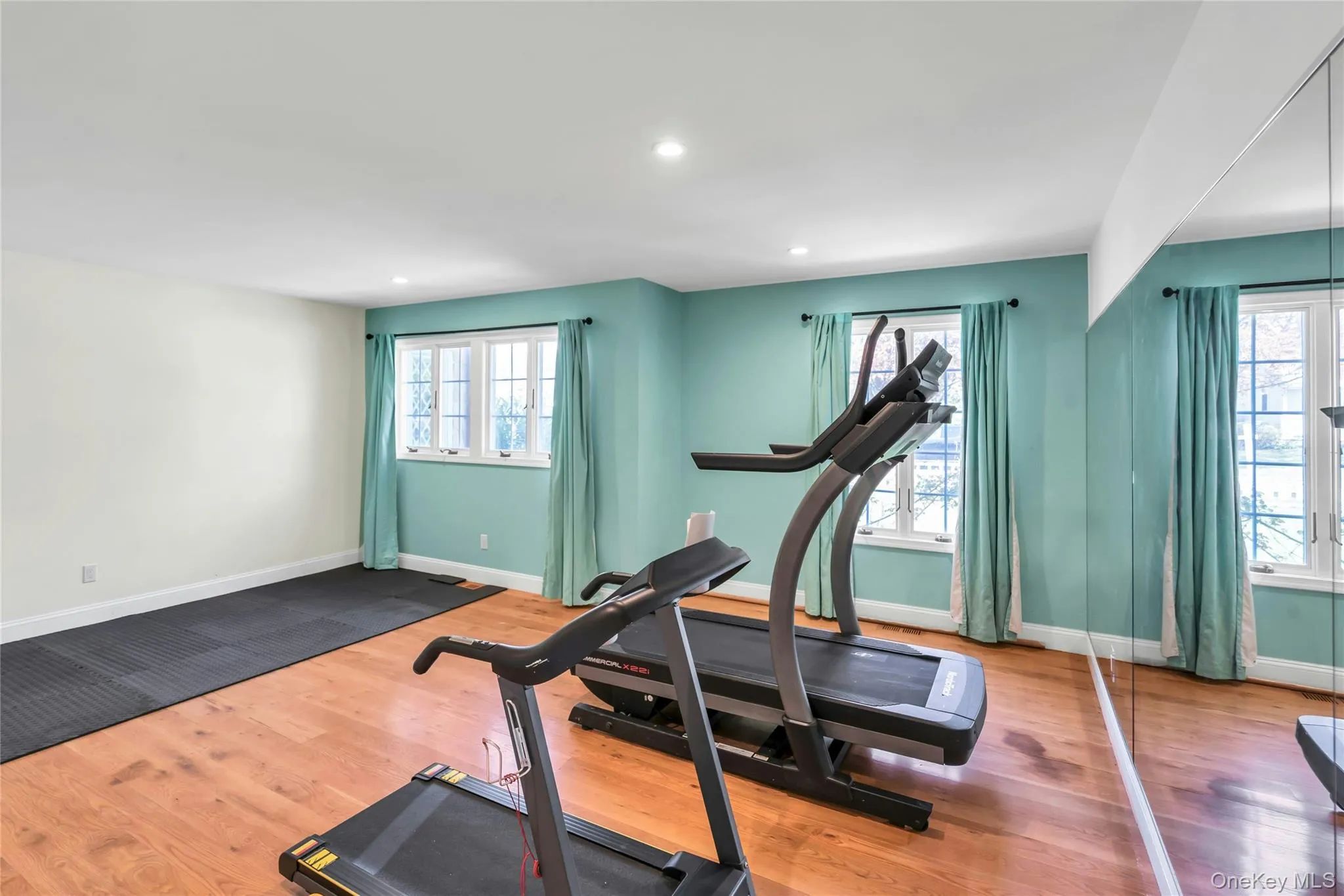 Room featuring light wood-finish flooring, recessed lighting, and a full mirrored wall Room featuring light wood-finish flooring, recessed lighting, and a full mirrored wall