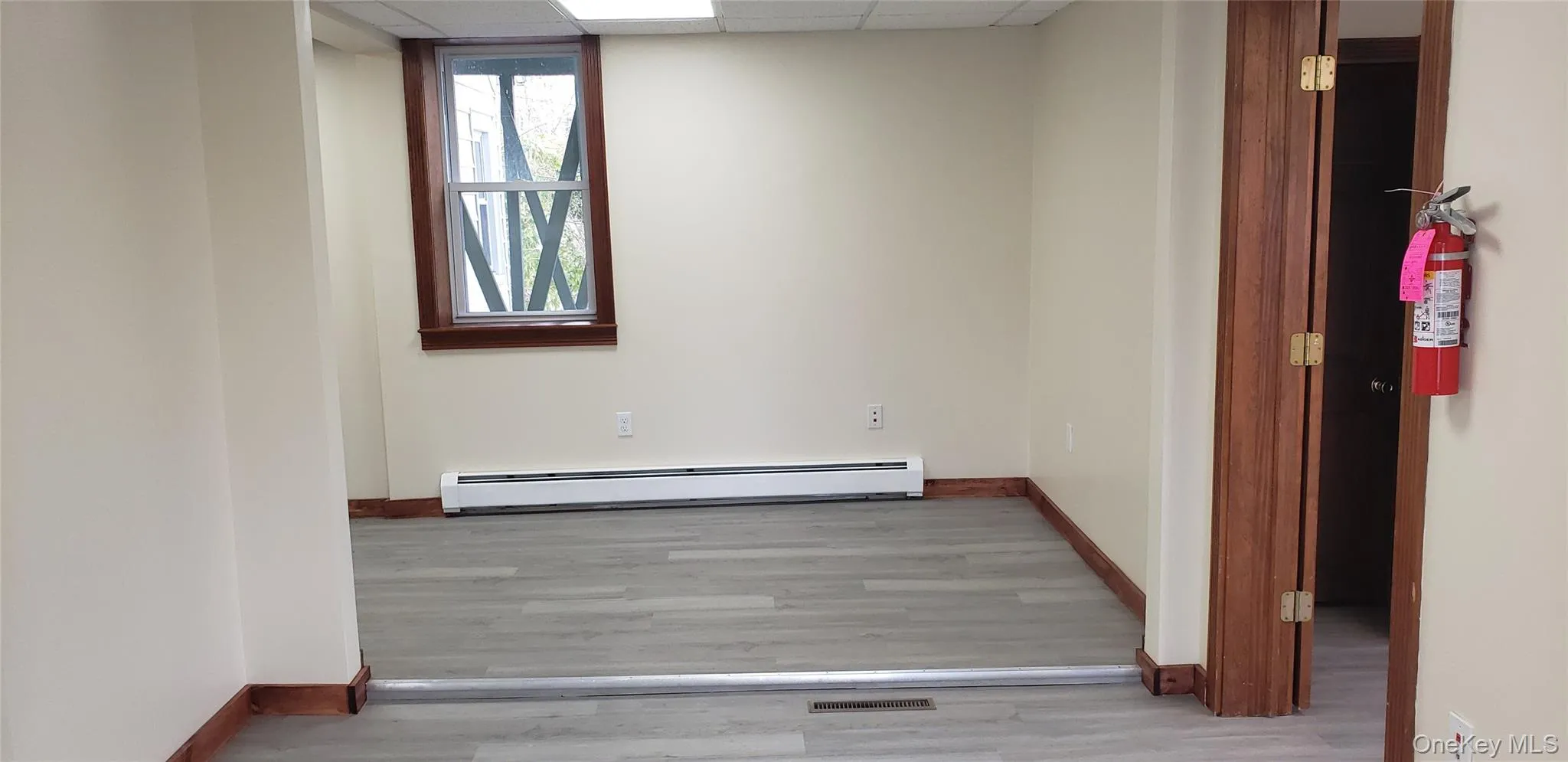 Spare room featuring a drop ceiling, baseboard heating, and wood finished floors Spare room featuring a drop ceiling, baseboard heating, and wood finished floors