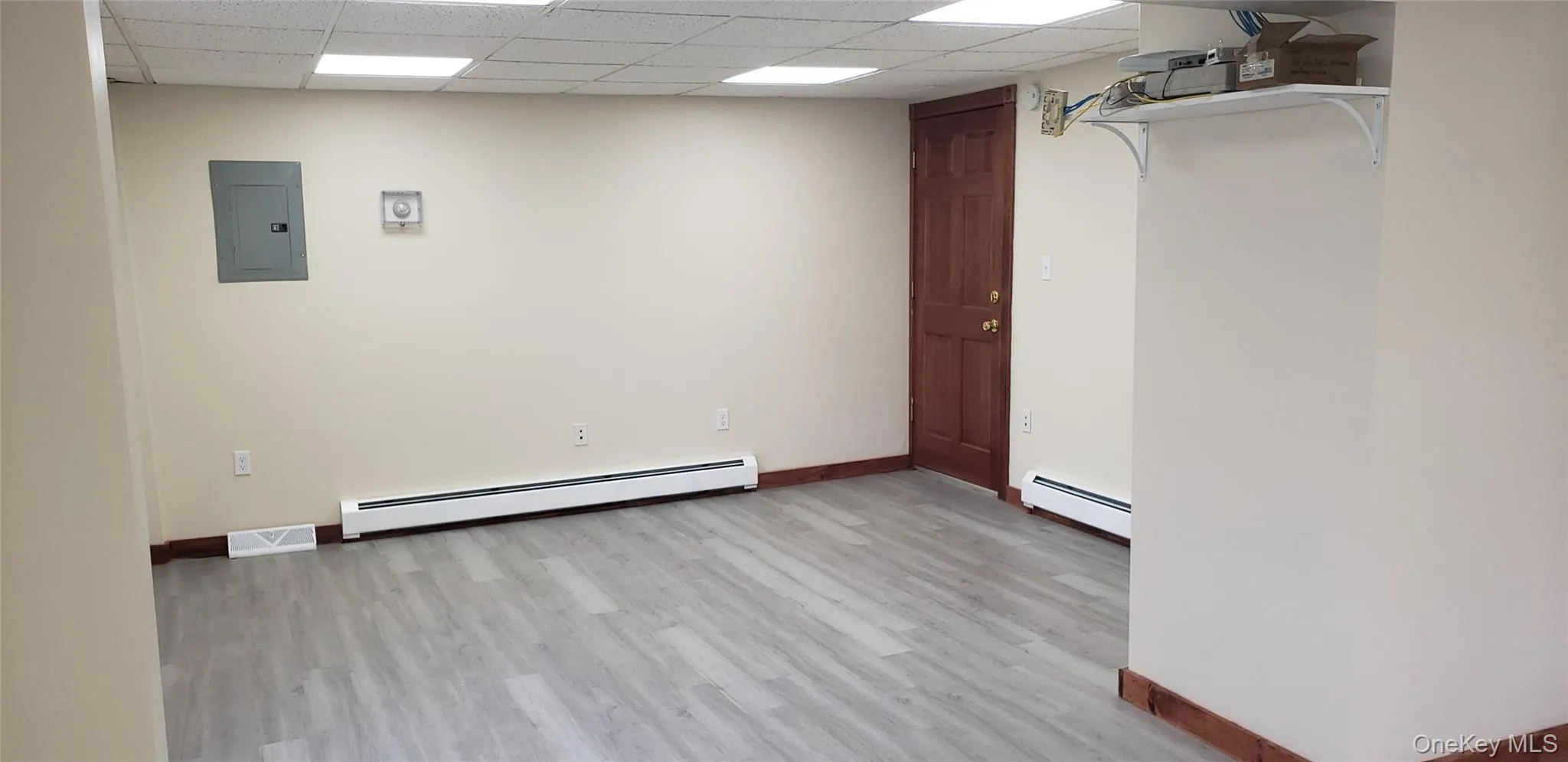 Unfurnished room featuring light wood-style flooring, baseboard heating, electric panel, and a paneled ceiling Unfurnished room featuring light wood-style flooring, baseboard heating, electric panel, and a paneled ceiling