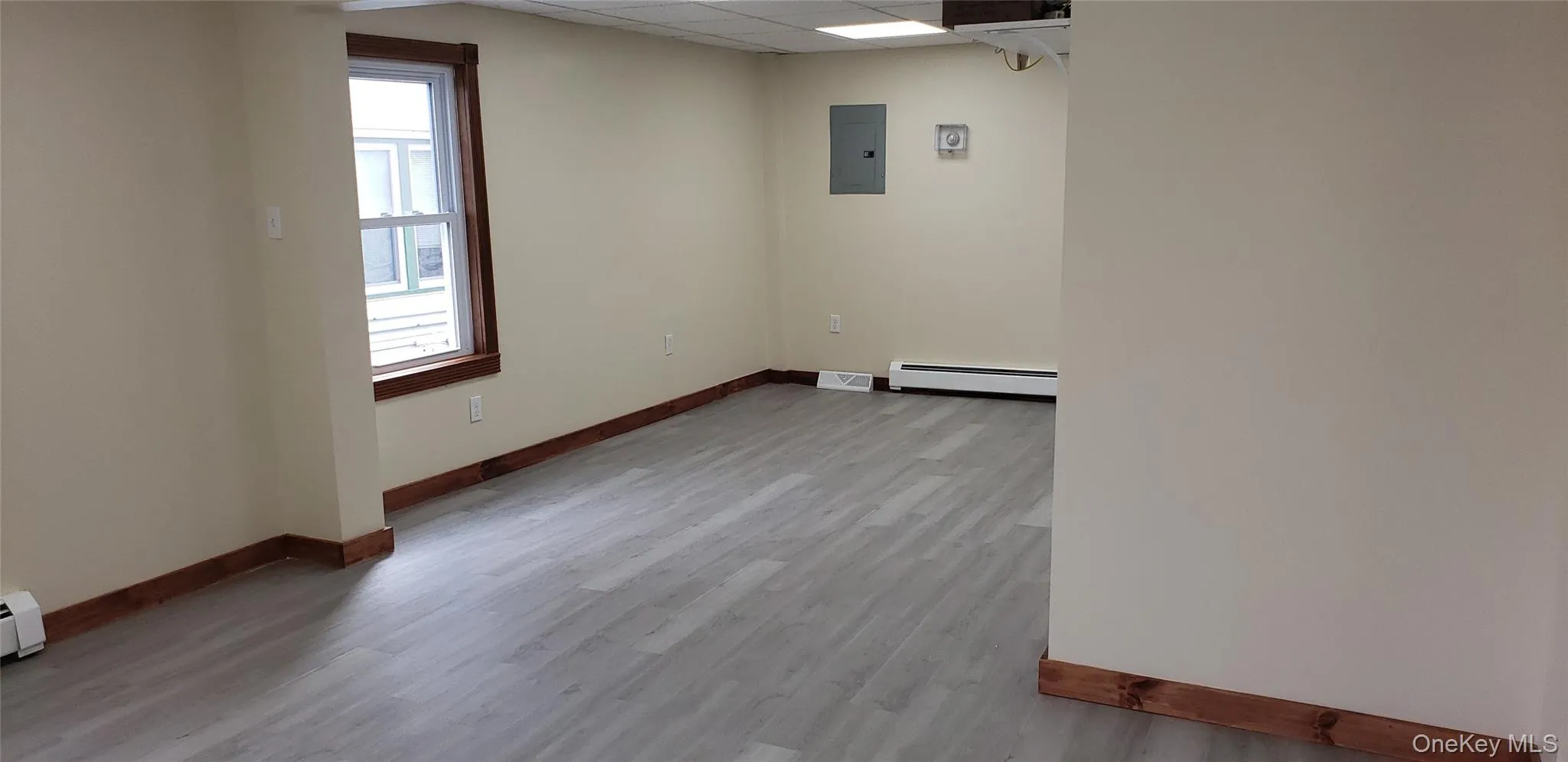 Empty room with a paneled ceiling, light wood-style floors, electric panel, and a baseboard radiator Empty room with a paneled ceiling, light wood-style floors, electric panel, and a baseboard radiator
