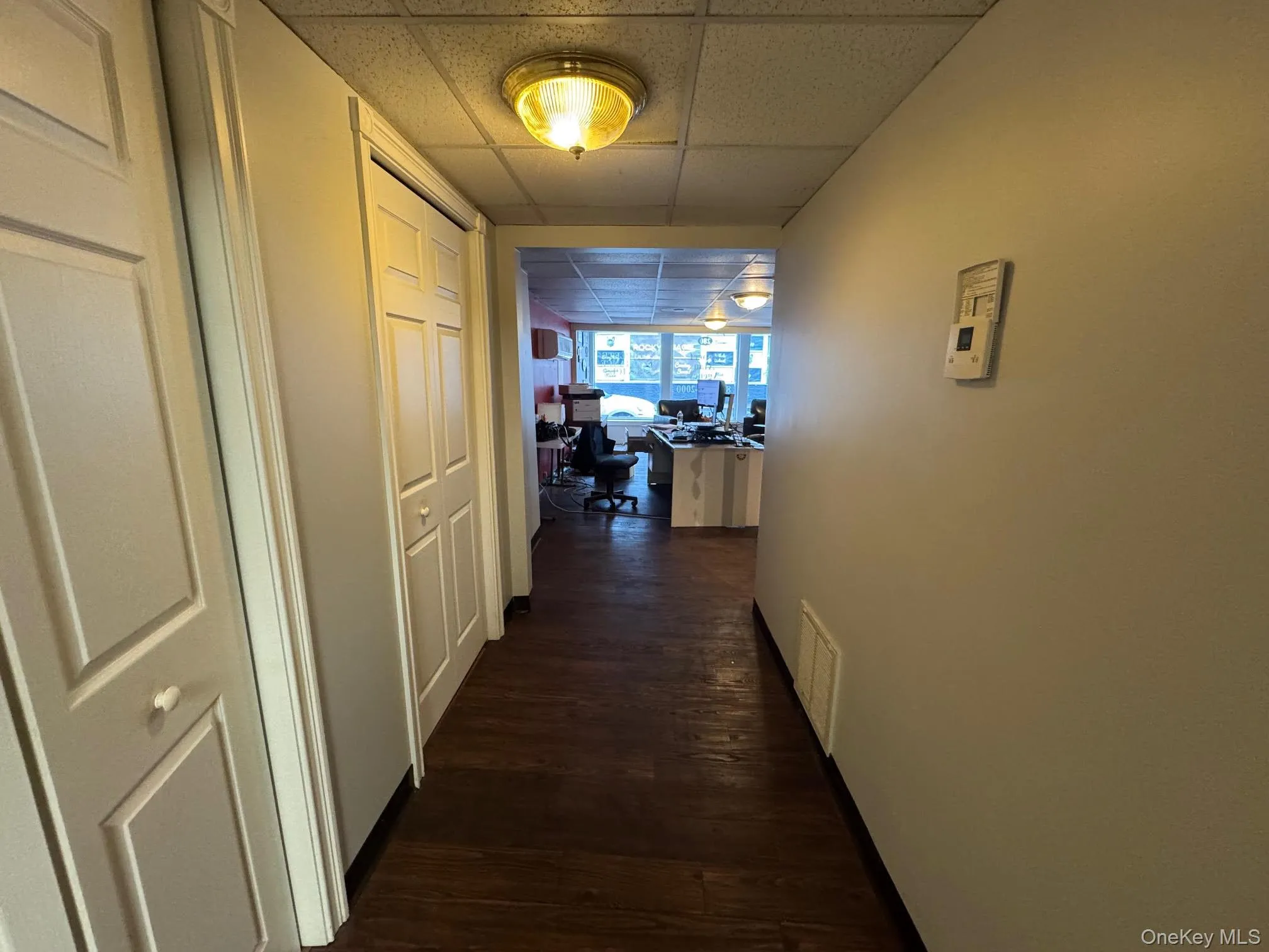 Hallway featuring a desk, a paneled ceiling, and dark wood-style flooring Hallway featuring a desk, a paneled ceiling, and dark wood-style flooring