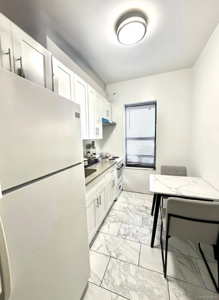 Kitchen with white appliances, white cabinetry, light countertops, and light marble finish flooring Kitchen with white appliances, white cabinetry, light countertops, and light marble finish flooring