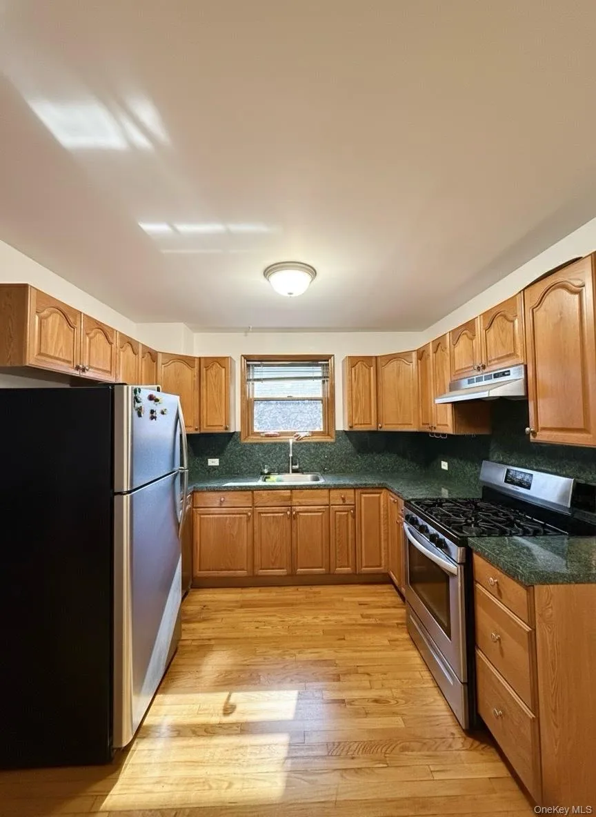 Kitchen with stainless steel appliances, decorative backsplash, dark stone counters, brown cabinets, and light wood-type flooring Kitchen with stainless steel appliances, decorative backsplash, dark stone counters, brown cabinets, and light wood-type flooring