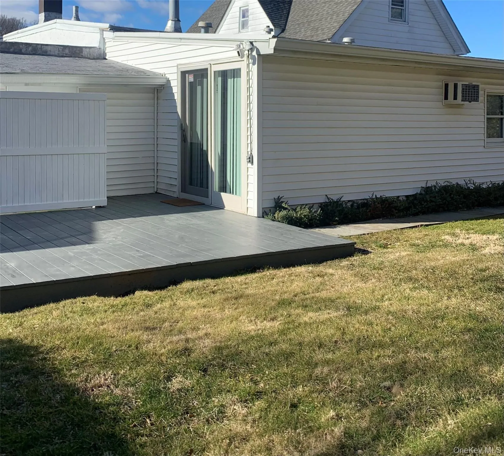 View of property exterior with a lawn, an AC wall unit, a shingled roof, and a deck View of property exterior with a lawn, an AC wall unit, a shingled roof, and a deck