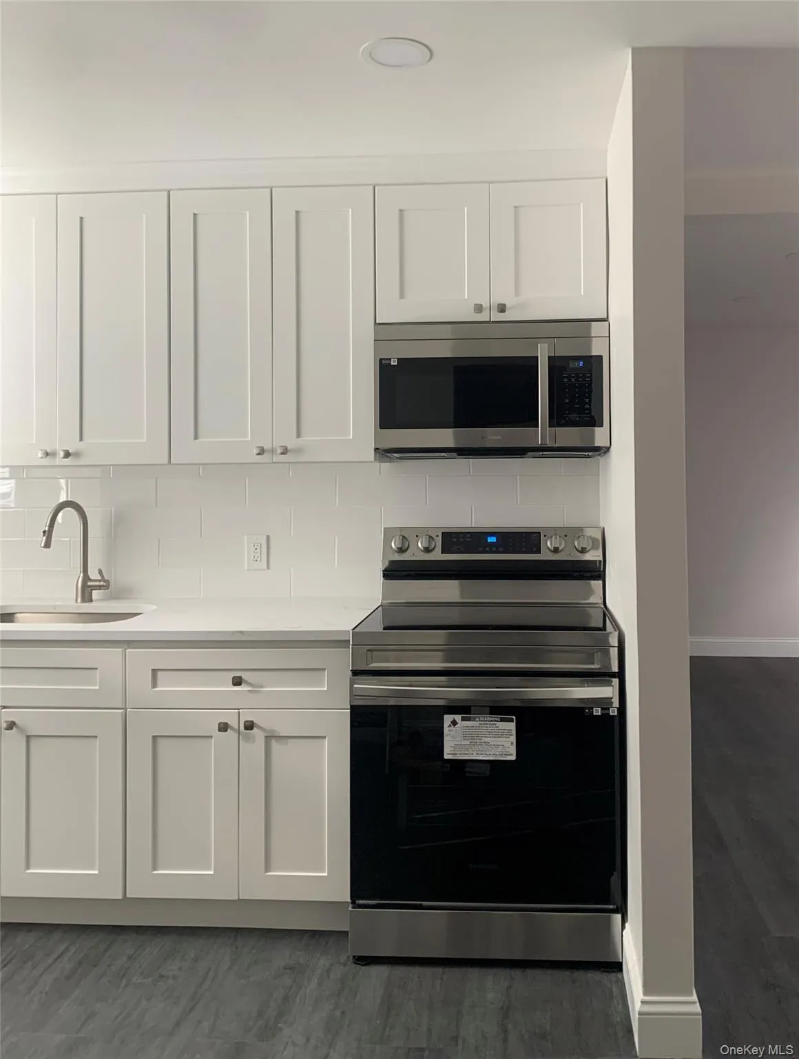 Kitchen featuring appliances with stainless steel finishes, white cabinets, decorative backsplash, light stone counters, and dark wood-style floors Kitchen featuring appliances with stainless steel finishes, white cabinets, decorative backsplash, light stone counters, and dark wood-style floors