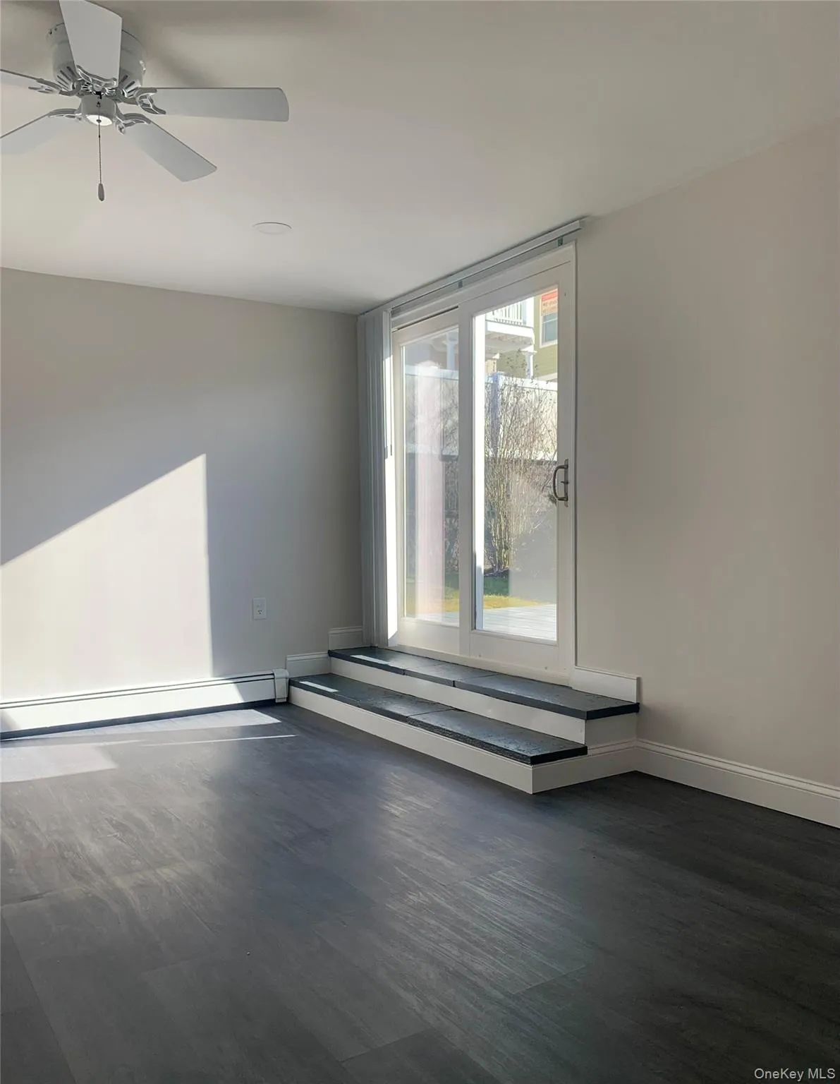 Unfurnished room with dark wood-style floors, baseboard heating, and a ceiling fan Unfurnished room with dark wood-style floors, baseboard heating, and a ceiling fan