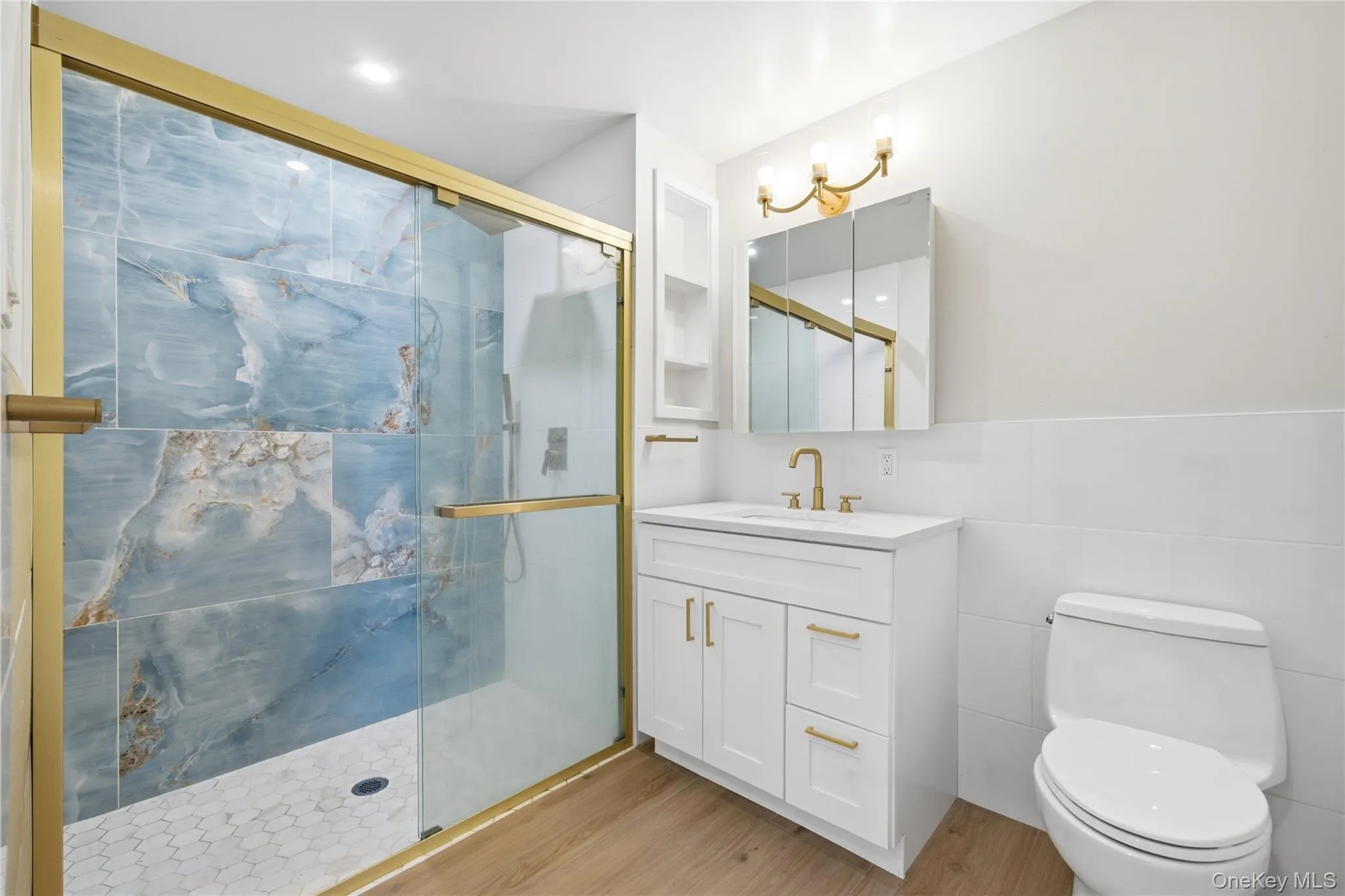 Bathroom featuring a marble finish shower, vanity, tile walls, and light wood-style floors Bathroom featuring a marble finish shower, vanity, tile walls, and light wood-style floors