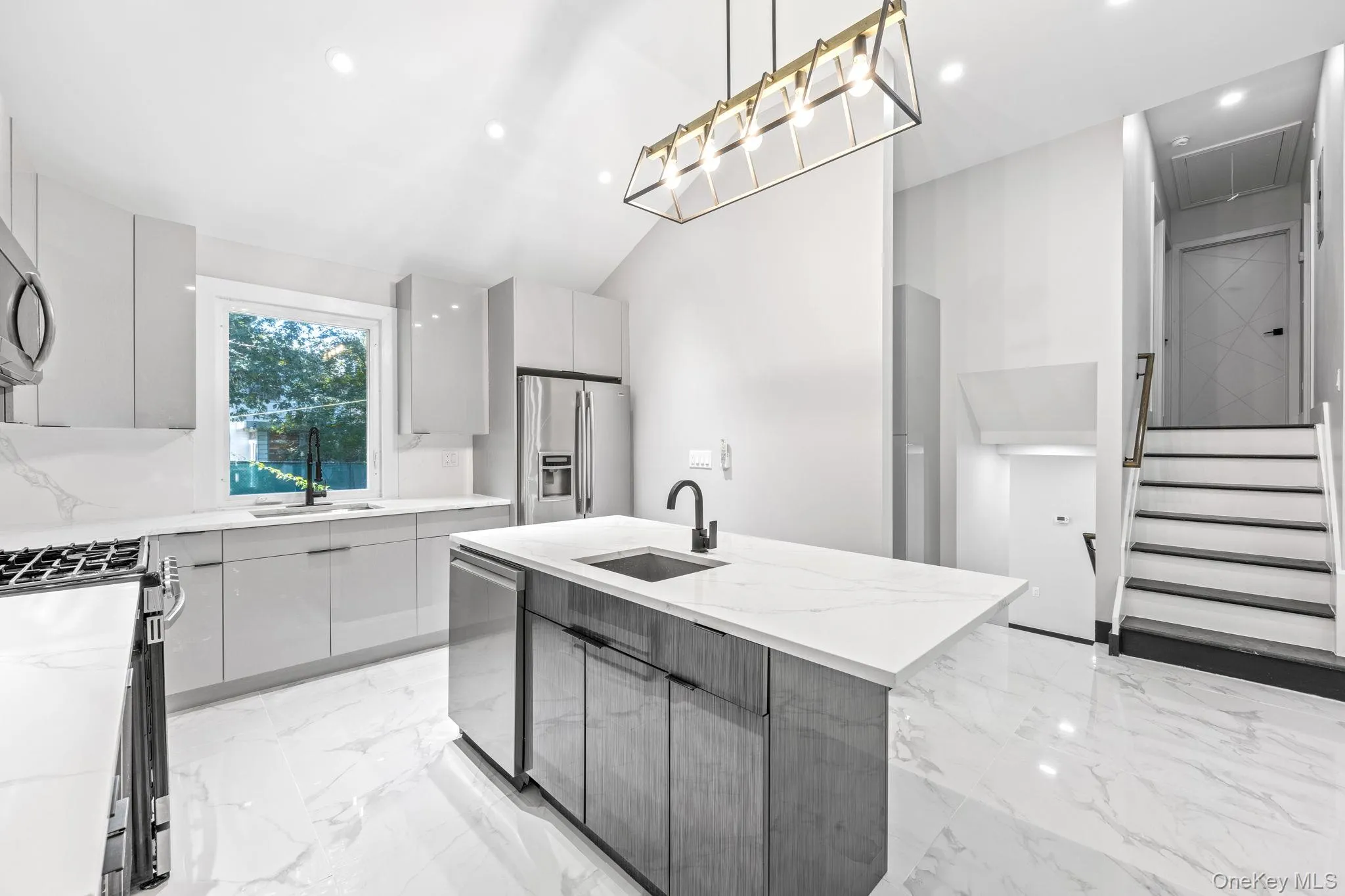 Kitchen with an island with sink, light marble finish floors, appliances with stainless steel finishes, modern cabinets, and light stone counters Kitchen with an island with sink, light marble finish floors, appliances with stainless steel finishes, modern cabinets, and light stone counters