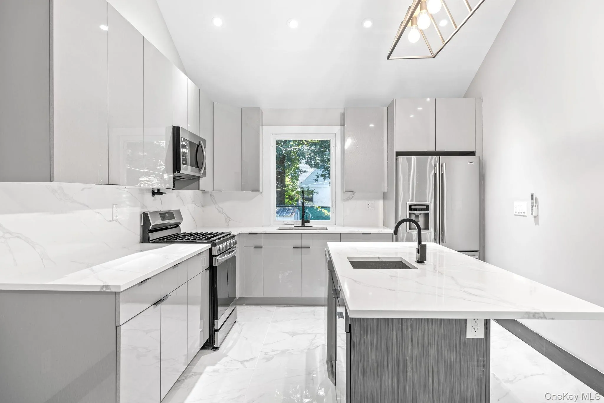 Kitchen featuring light marble finish floors, light stone counters, an island with sink, stainless steel appliances, and modern cabinets Kitchen featuring light marble finish floors, light stone counters, an island with sink, stainless steel appliances, and modern cabinets