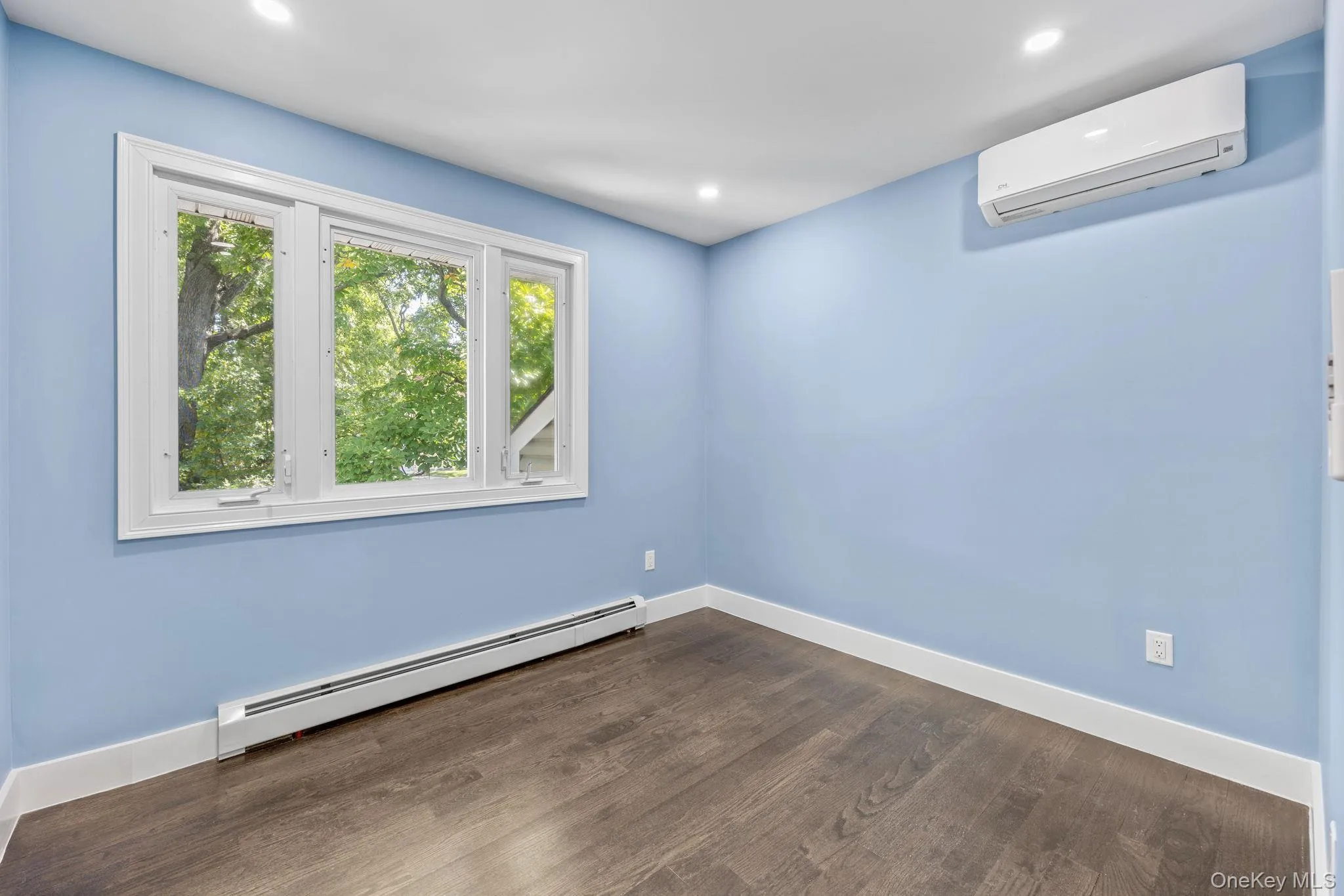 Spare room with a baseboard radiator, an AC wall unit, dark wood-style flooring, and recessed lighting Spare room with a baseboard radiator, an AC wall unit, dark wood-style flooring, and recessed lighting
