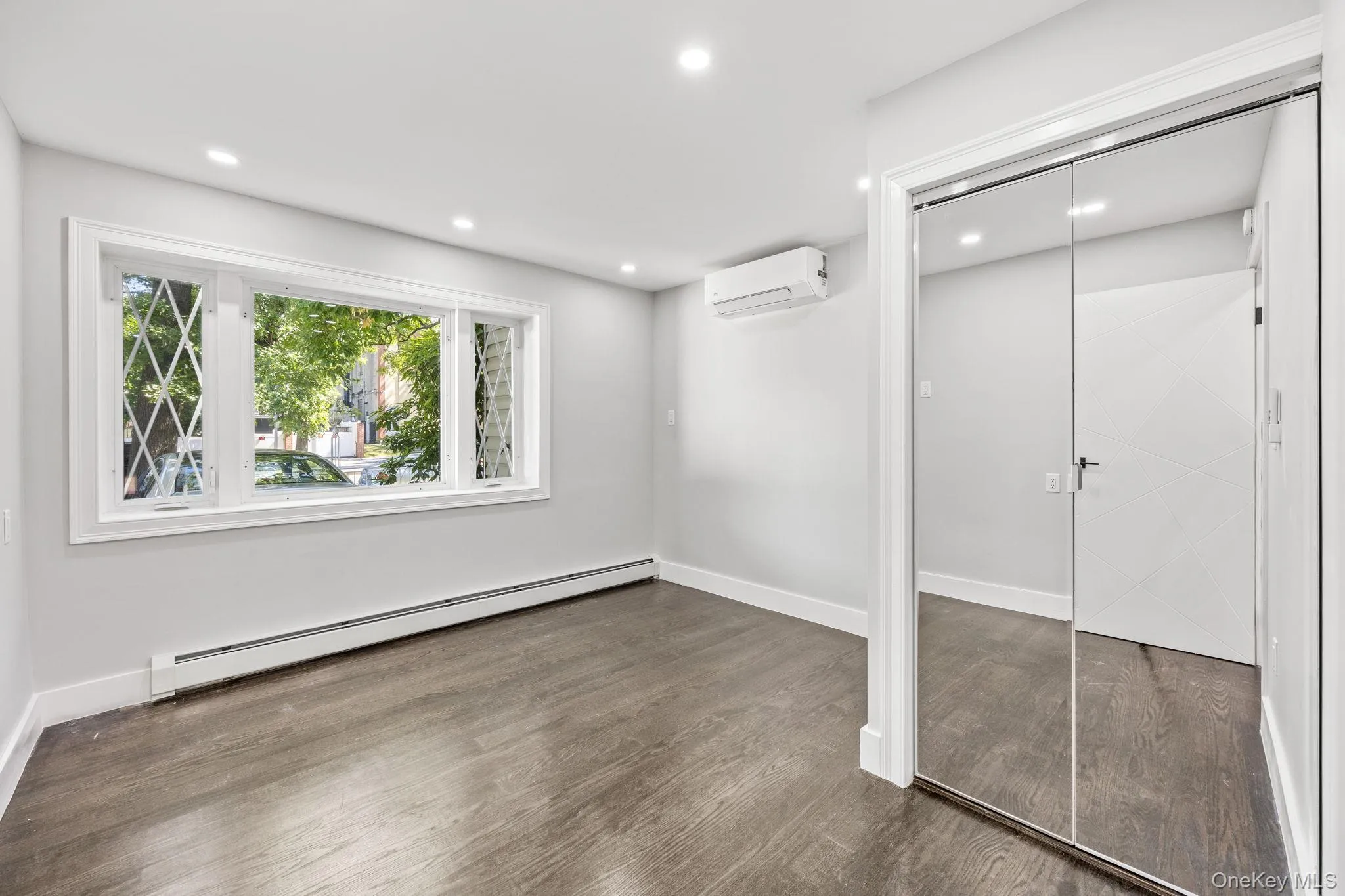 Unfurnished bedroom with a baseboard heating unit, recessed lighting, dark wood-style flooring, a closet, and an AC wall unit Unfurnished bedroom with a baseboard heating unit, recessed lighting, dark wood-style flooring, a closet, and an AC wall unit