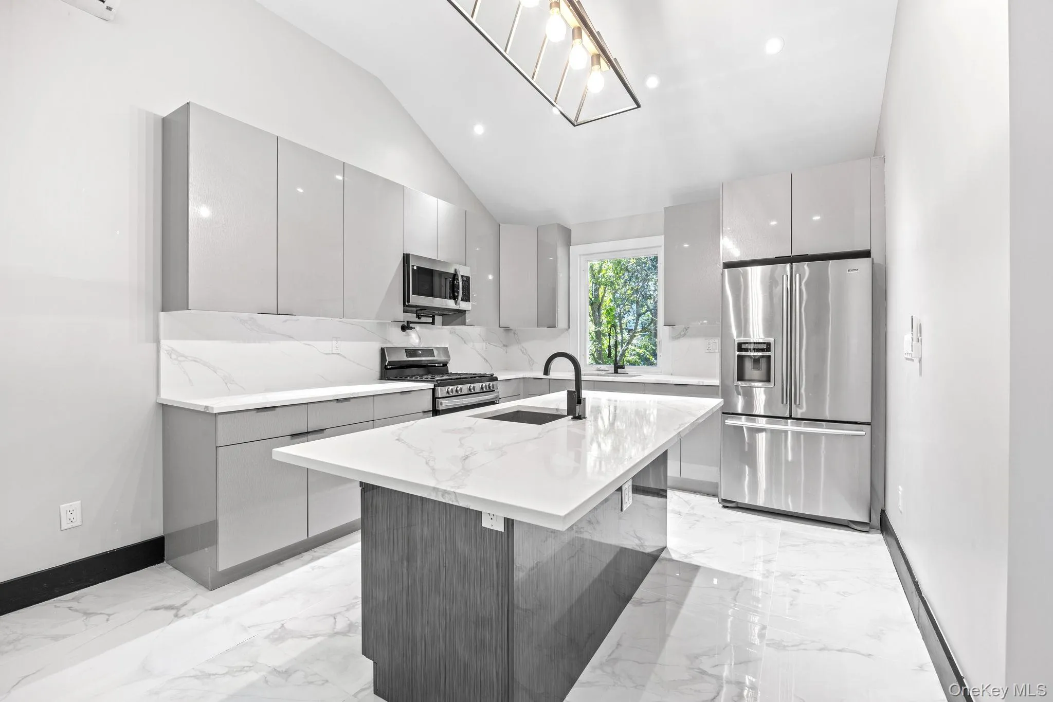 Kitchen with modern cabinets, stainless steel appliances, light stone counters, a kitchen island with sink, and lofted ceiling Kitchen with modern cabinets, stainless steel appliances, light stone counters, a kitchen island with sink, and lofted ceiling