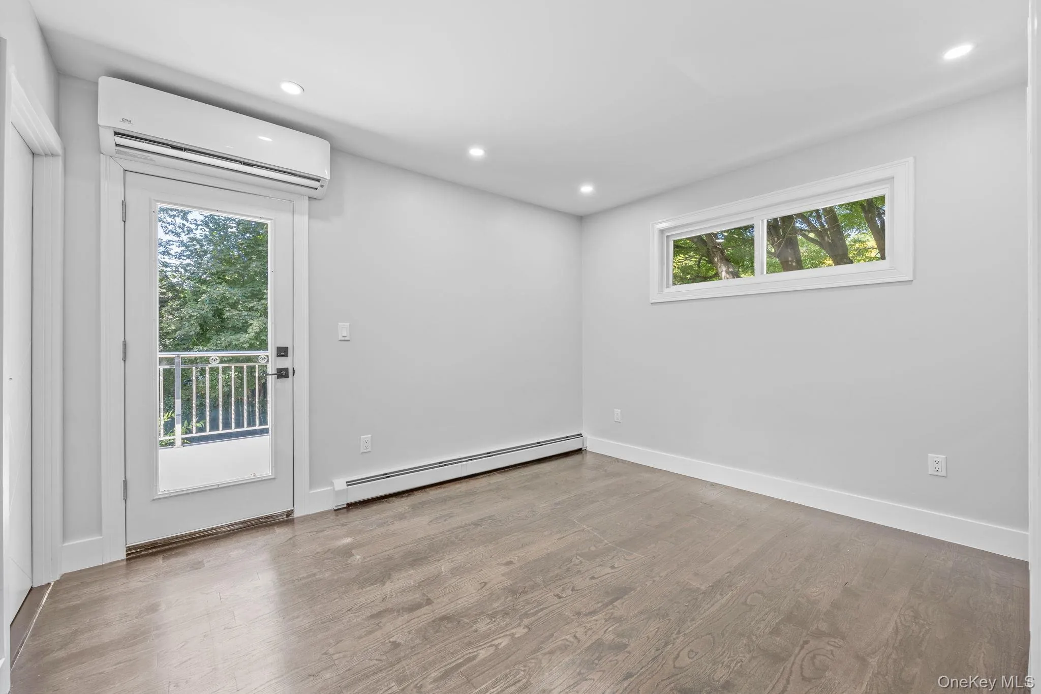 Empty room featuring recessed lighting, baseboard heating, a wall mounted AC, and light wood-style floors Empty room featuring recessed lighting, baseboard heating, a wall mounted AC, and light wood-style floors