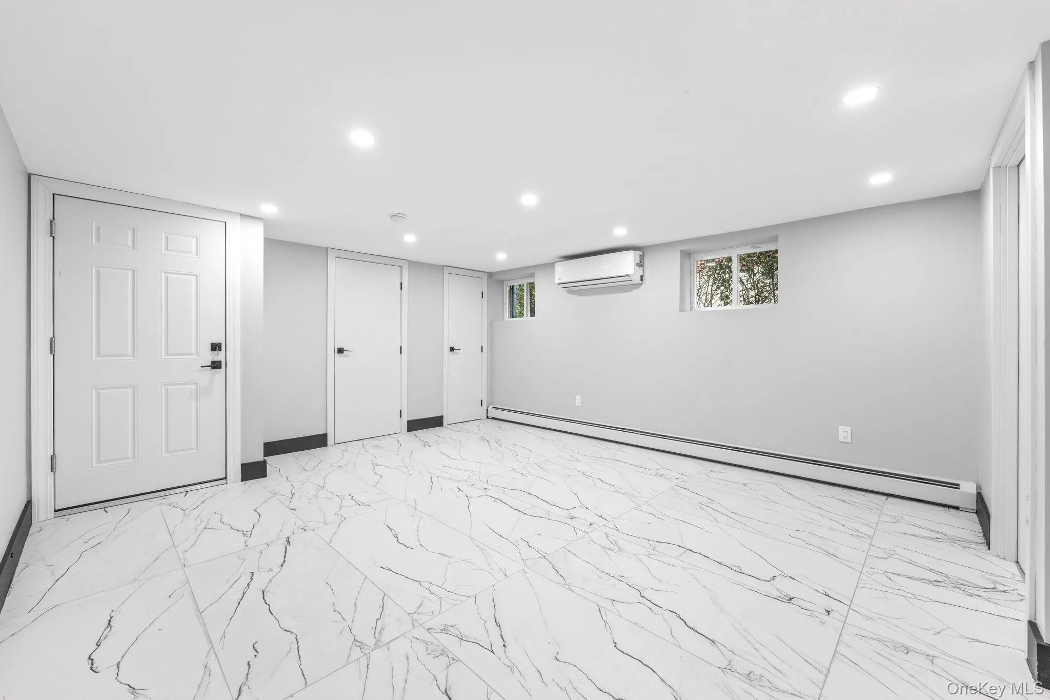 Below grade area featuring light marble finish flooring, recessed lighting, baseboard heating, and a wall mounted air conditioner Below grade area featuring light marble finish flooring, recessed lighting, baseboard heating, and a wall mounted air conditioner