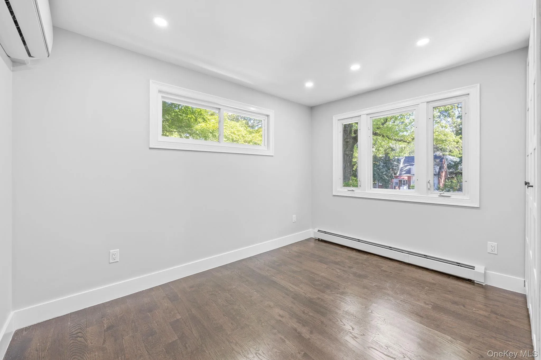 Empty room featuring baseboard heating, a wall unit AC, plenty of natural light, recessed lighting, and dark wood finished floors Empty room featuring baseboard heating, a wall unit AC, plenty of natural light, recessed lighting, and dark wood finished floors