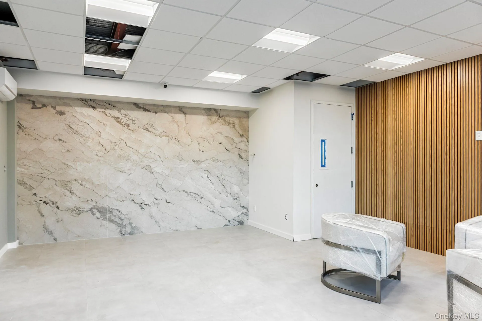 Below grade area featuring a drop ceiling, wooden walls, and a wall unit AC Below grade area featuring a drop ceiling, wooden walls, and a wall unit AC