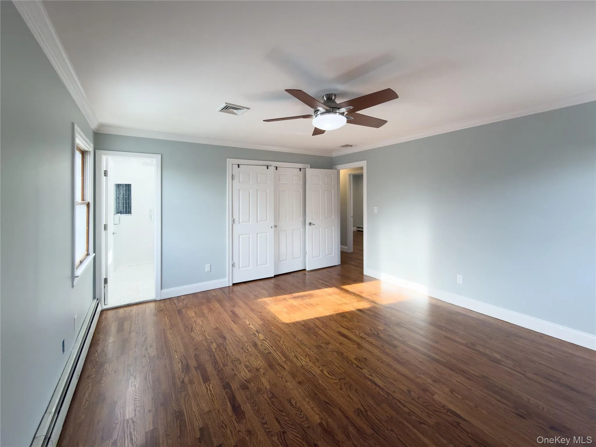 Unfurnished bedroom featuring a baseboard heating unit, ornamental molding, dark wood-style floors, a closet, and a ceiling fan Unfurnished bedroom featuring a baseboard heating unit, ornamental molding, dark wood-style floors, a closet, and a ceiling fan
