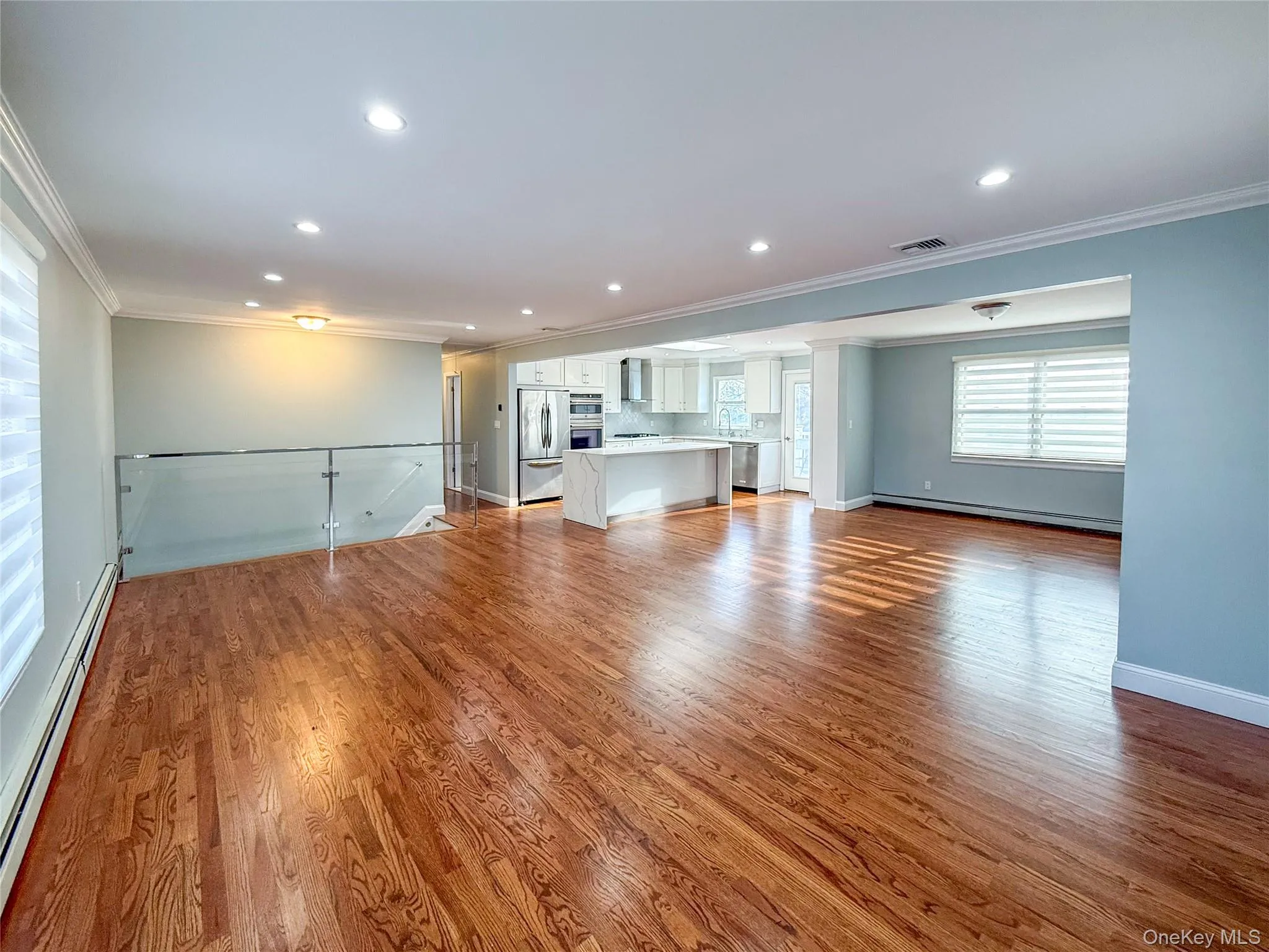 Unfurnished living room featuring a baseboard radiator, ornamental molding, dark wood finished floors, and recessed lighting Unfurnished living room featuring a baseboard radiator, ornamental molding, dark wood finished floors, and recessed lighting