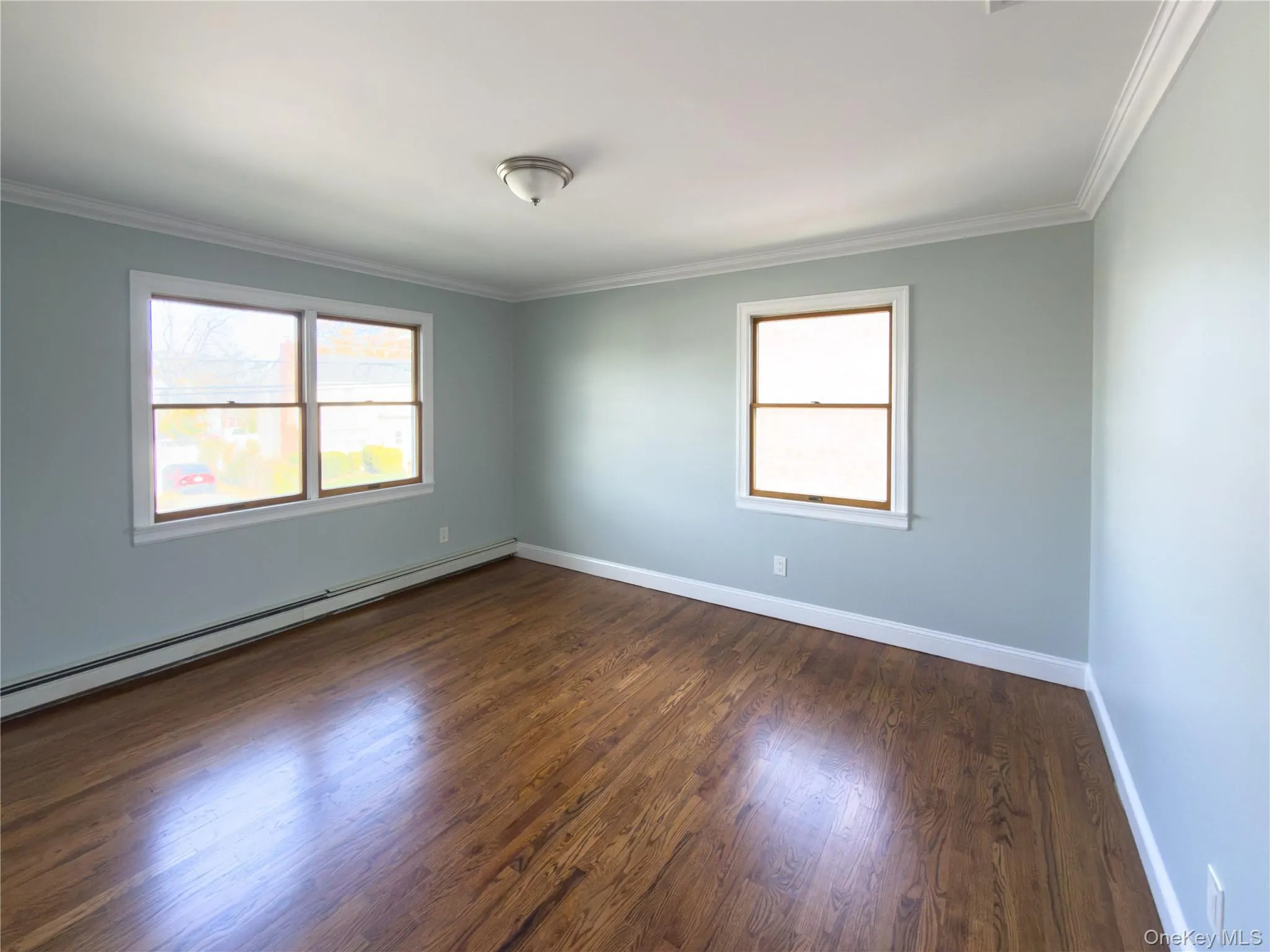 Empty room with baseboard heating, crown molding, healthy amount of natural light, and dark wood-type flooring Empty room with baseboard heating, crown molding, healthy amount of natural light, and dark wood-type flooring