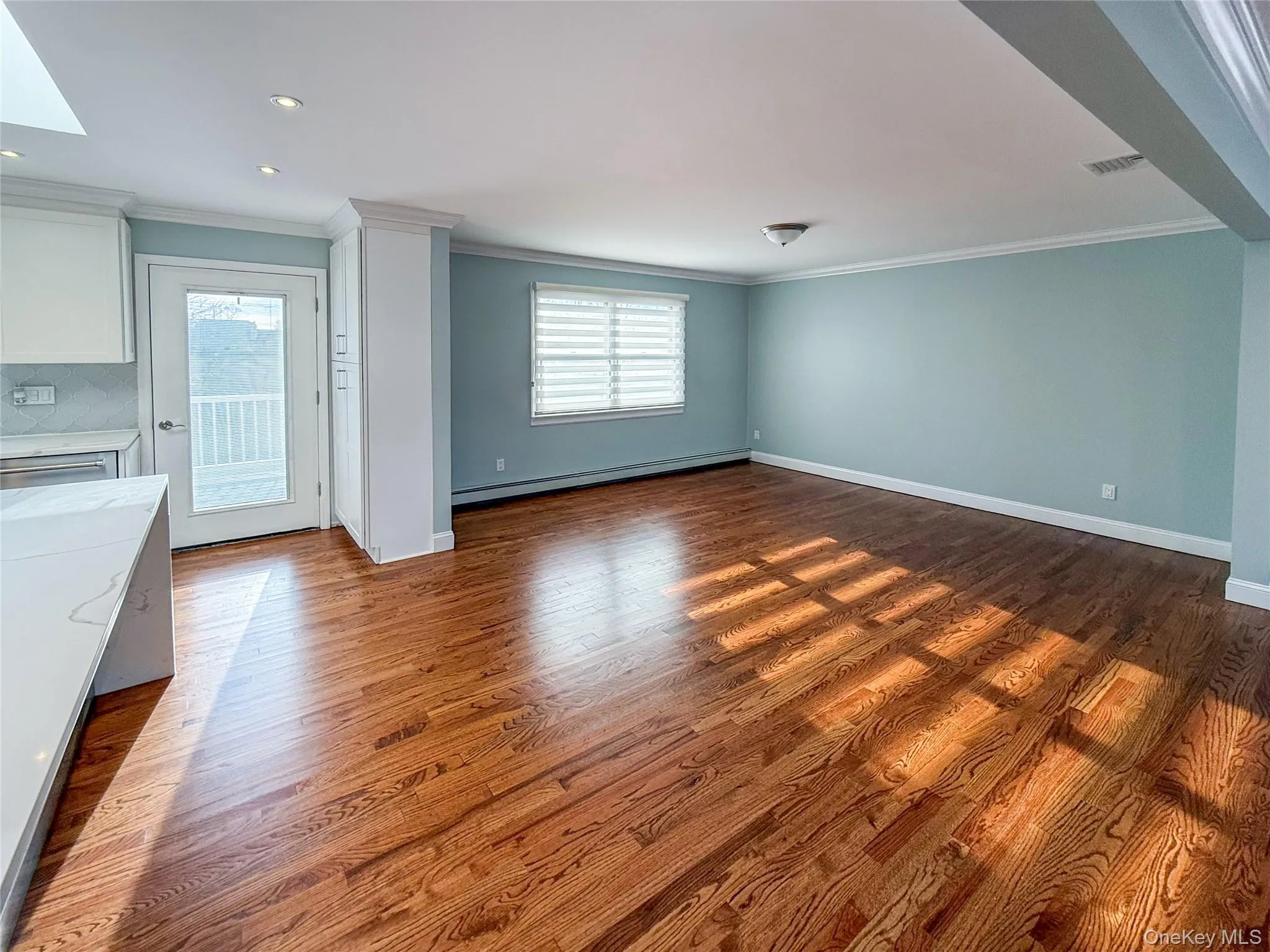 Unfurnished living room featuring crown molding, dark wood-style flooring, a baseboard radiator, and recessed lighting Unfurnished living room featuring crown molding, dark wood-style flooring, a baseboard radiator, and recessed lighting