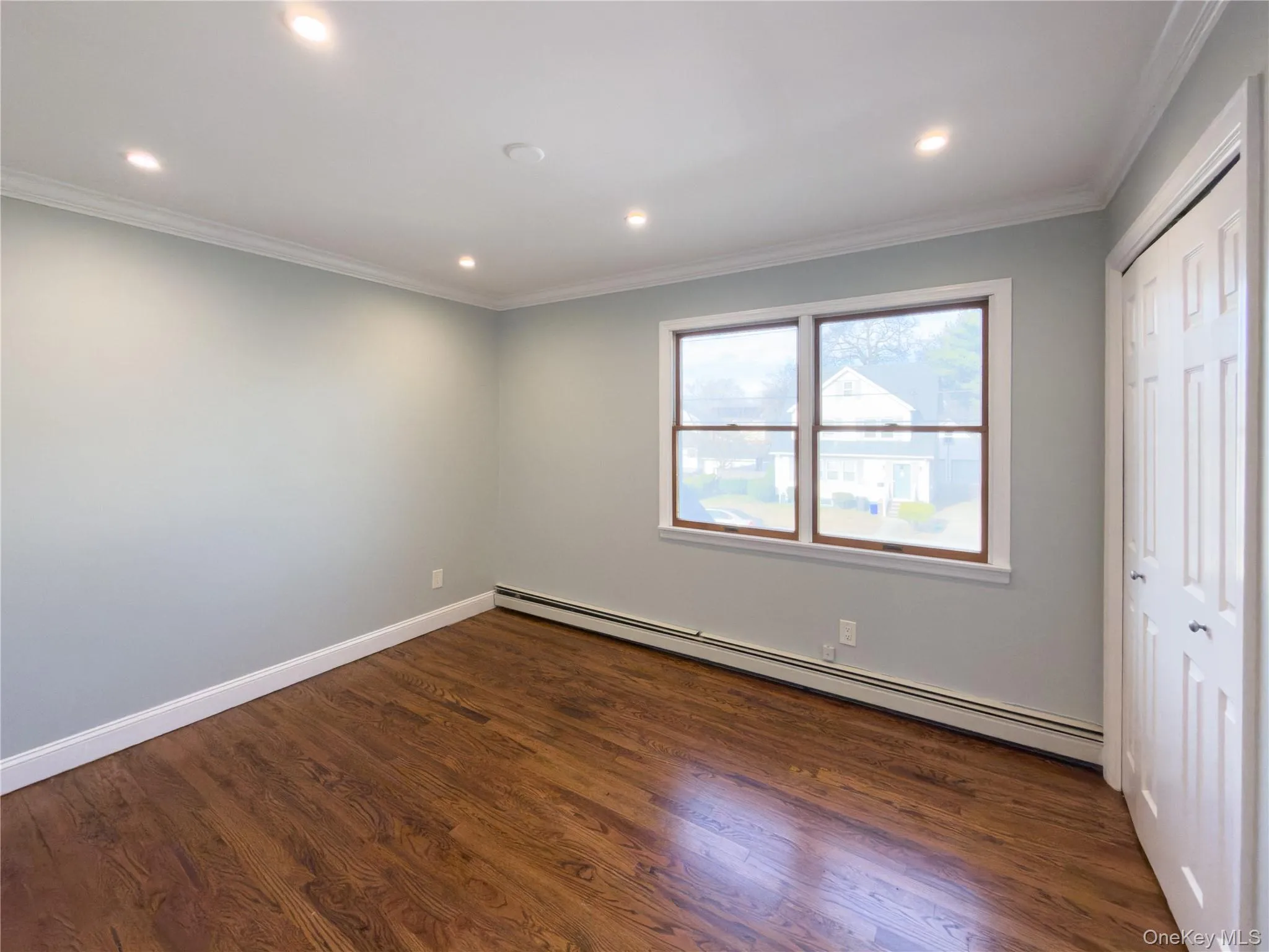 Unfurnished bedroom with a baseboard radiator, dark wood finished floors, crown molding, a closet, and recessed lighting Unfurnished bedroom with a baseboard radiator, dark wood finished floors, crown molding, a closet, and recessed lighting