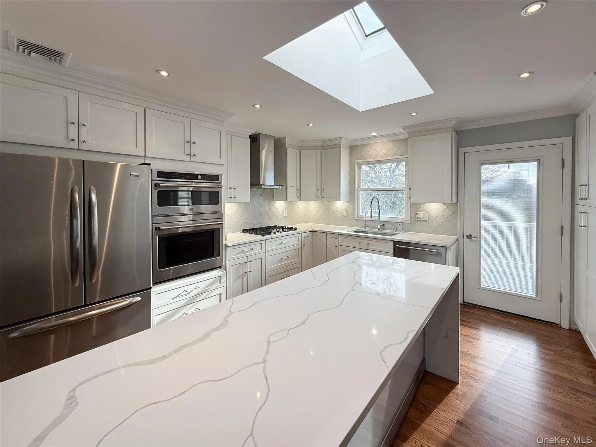 Kitchen with appliances with stainless steel finishes, white cabinetry, light stone counters, ornamental molding, and dark wood-style floors Kitchen with appliances with stainless steel finishes, white cabinetry, light stone counters, ornamental molding, and dark wood-style floors