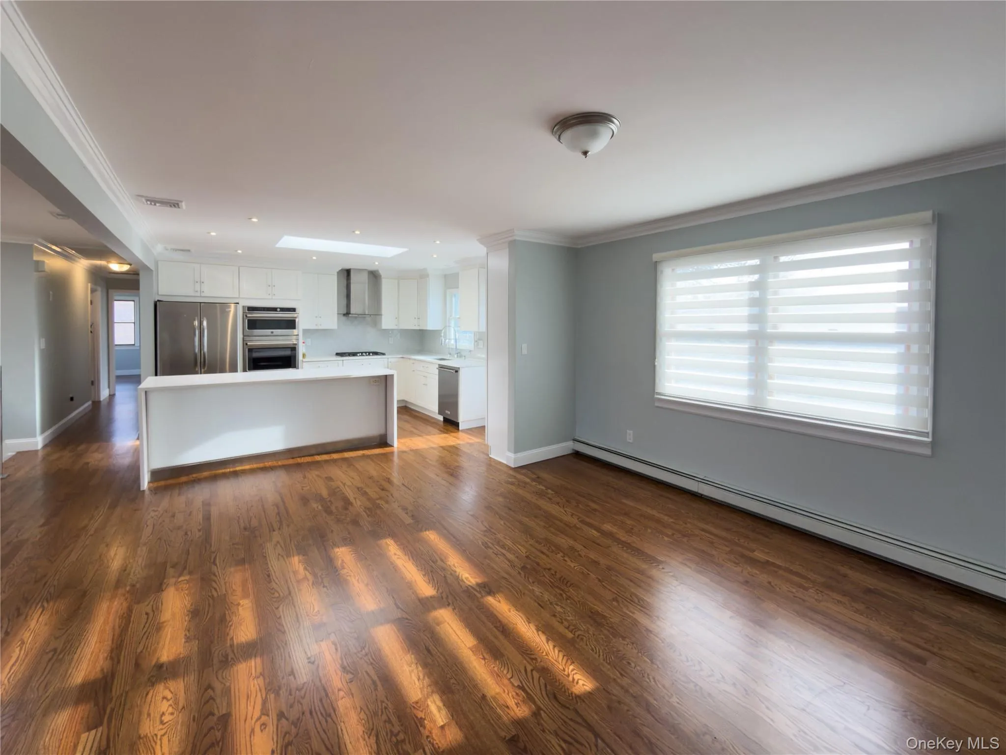 Kitchen featuring crown molding, open floor plan, white cabinets, light countertops, and a baseboard heating unit Kitchen featuring crown molding, open floor plan, white cabinets, light countertops, and a baseboard heating unit