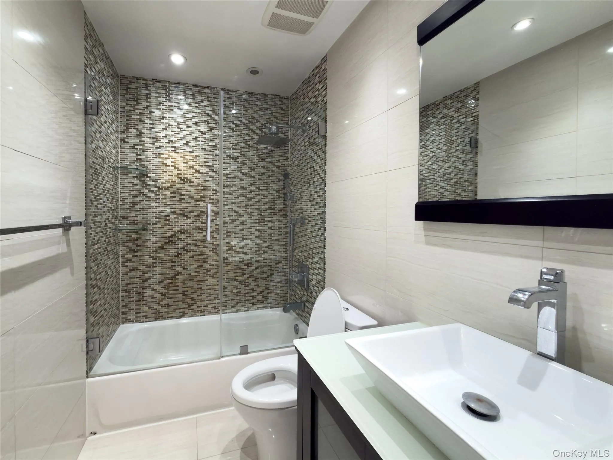Bathroom featuring tile walls, vanity, shower / bath combination with glass door, tile patterned flooring, and recessed lighting Bathroom featuring tile walls, vanity, shower / bath combination with glass door, tile patterned flooring, and recessed lighting
