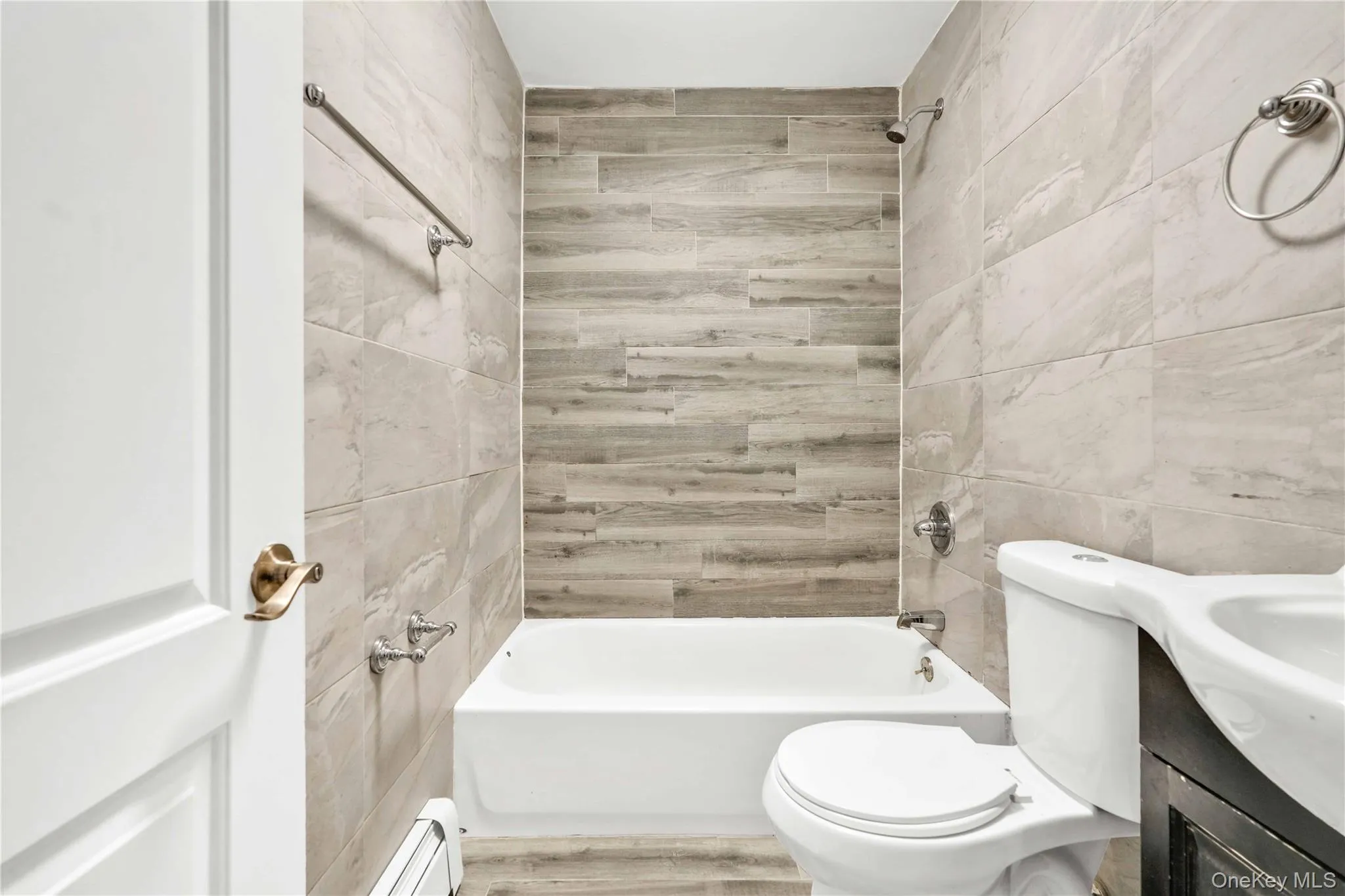 Full bathroom with shower / bathing tub combination, vanity, tile walls, a baseboard heating unit, and toilet Full bathroom with shower / bathing tub combination, vanity, tile walls, a baseboard heating unit, and toilet