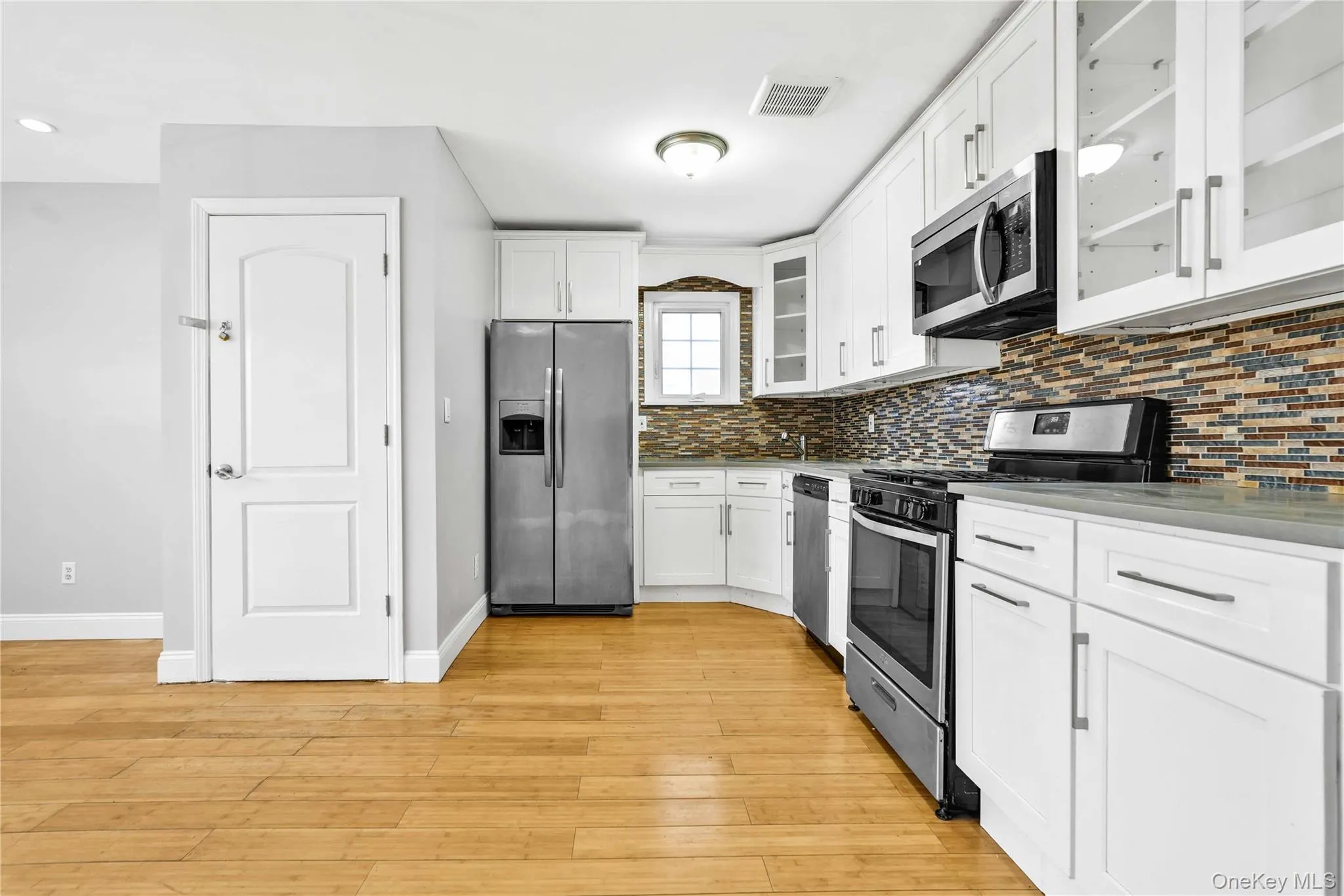 Kitchen featuring backsplash, white cabinetry, appliances with stainless steel finishes, light wood-style flooring, and visible vents Kitchen featuring backsplash, white cabinetry, appliances with stainless steel finishes, light wood-style flooring, and visible vents