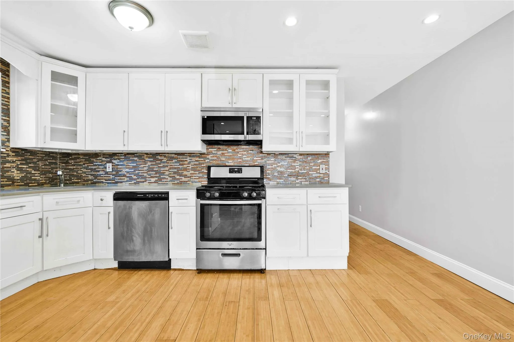 Kitchen featuring light countertops, stainless steel appliances, baseboards, decorative backsplash, and light wood finished floors Kitchen featuring light countertops, stainless steel appliances, baseboards, decorative backsplash, and light wood finished floors