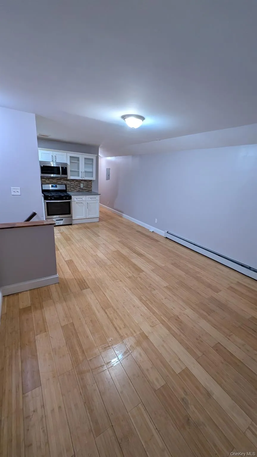 Kitchen featuring glass insert cabinets, white cabinets, a baseboard heating unit, appliances with stainless steel finishes, and light wood-type flooring Kitchen featuring glass insert cabinets, white cabinets, a baseboard heating unit, appliances with stainless steel finishes, and light wood-type flooring