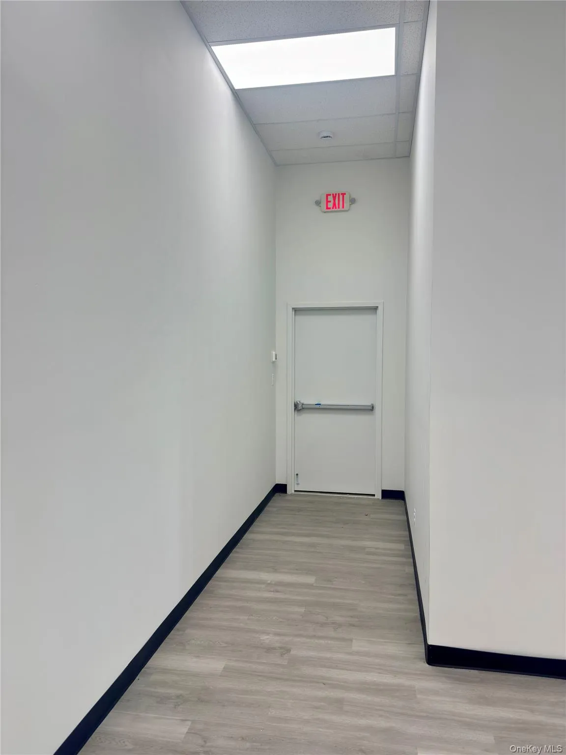 Hallway featuring light wood-type flooring and a drop ceiling Hallway featuring light wood-type flooring and a drop ceiling