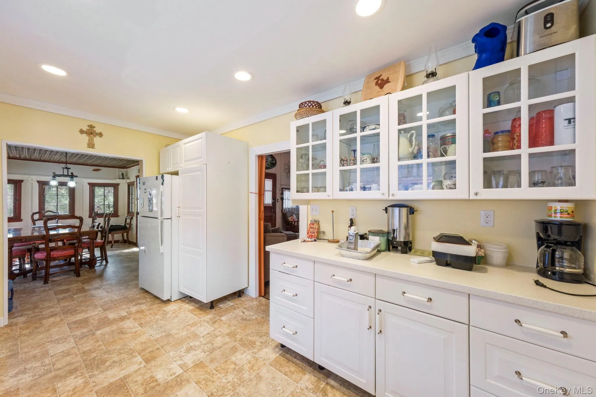 Kitchen with glass fronted cabinets, white cabinets, freestanding refrigerator, crown molding, and recessed lighting Kitchen with glass fronted cabinets, white cabinets, freestanding refrigerator, crown molding, and recessed lighting